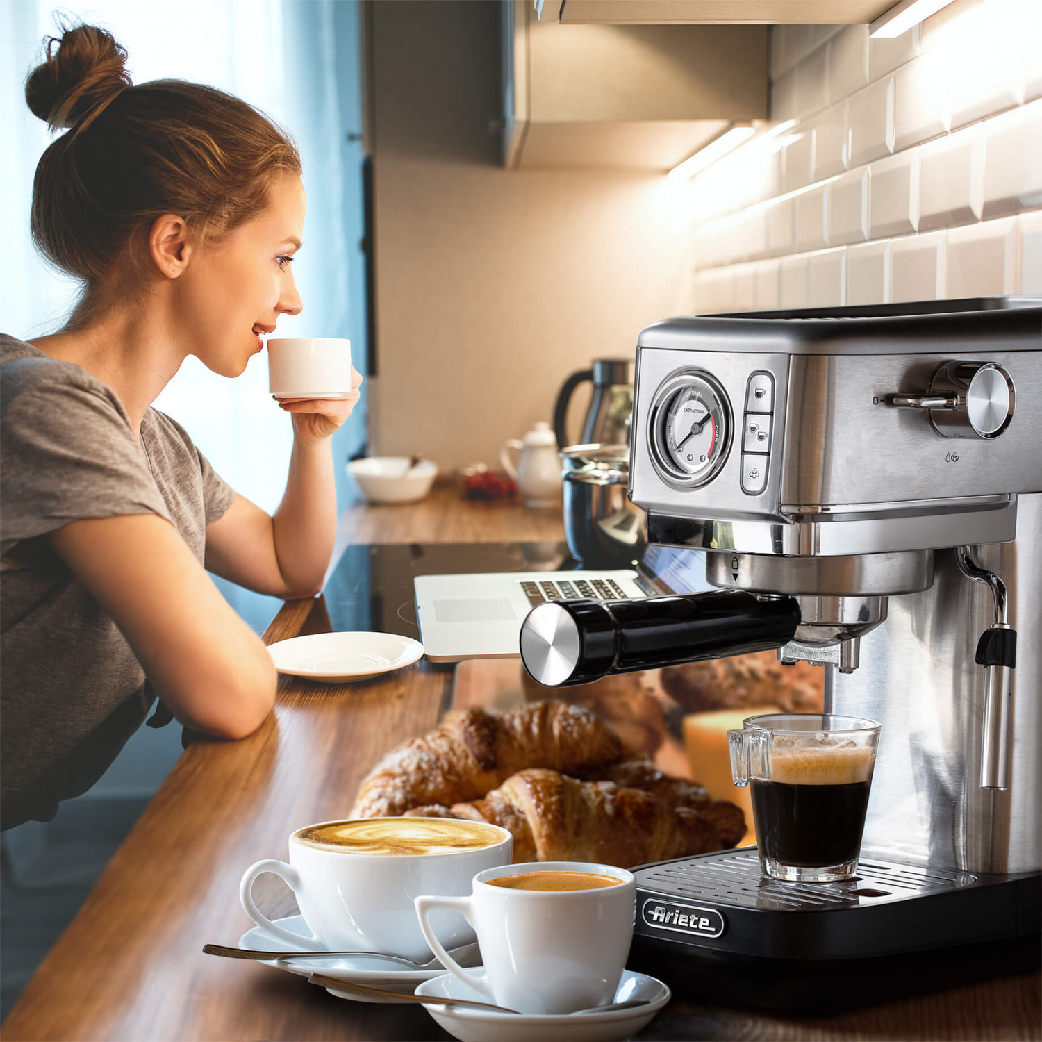 Una donna siede a un bancone da cucina in legno bevendo caffè accanto a una macchina per espresso e dolci.