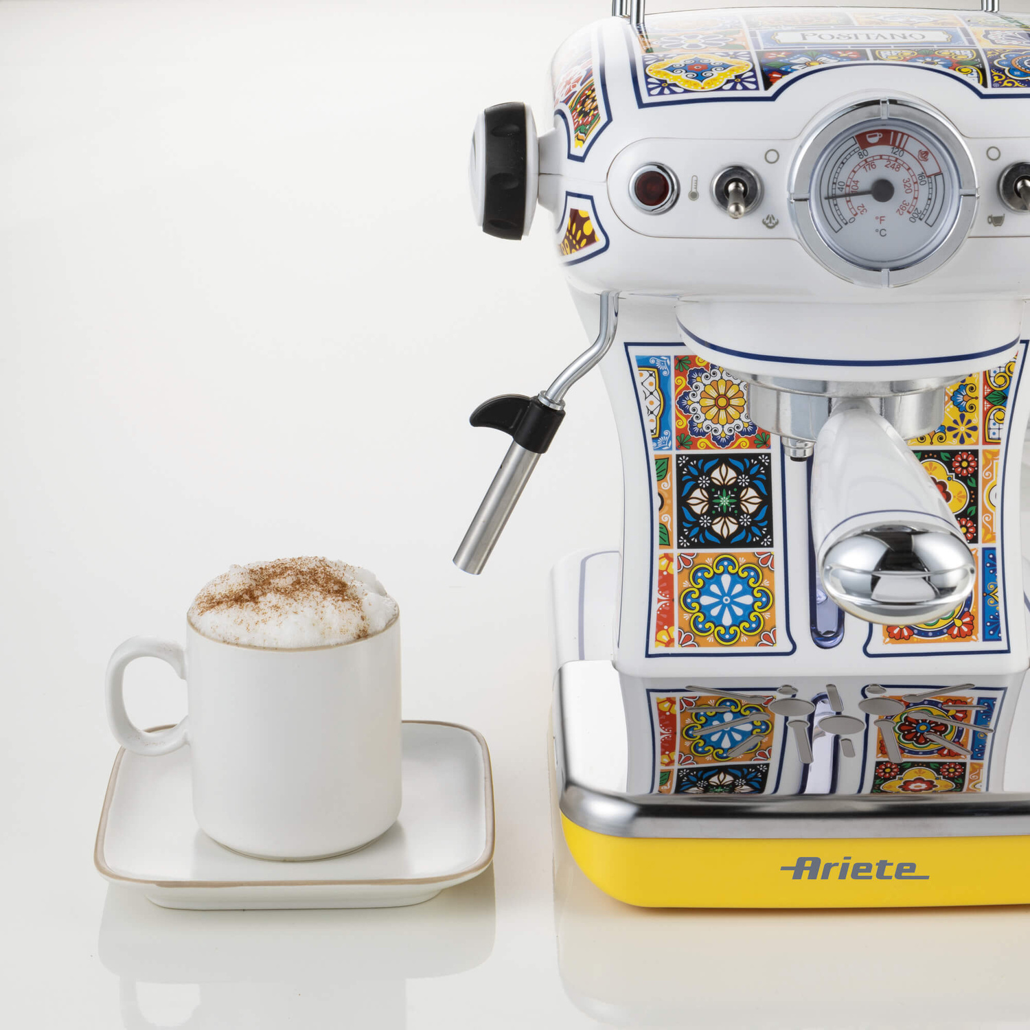 Una colorata macchina da caffè espresso Ariete e una tazza bianca di cappuccino con cannella su sfondo bianco.