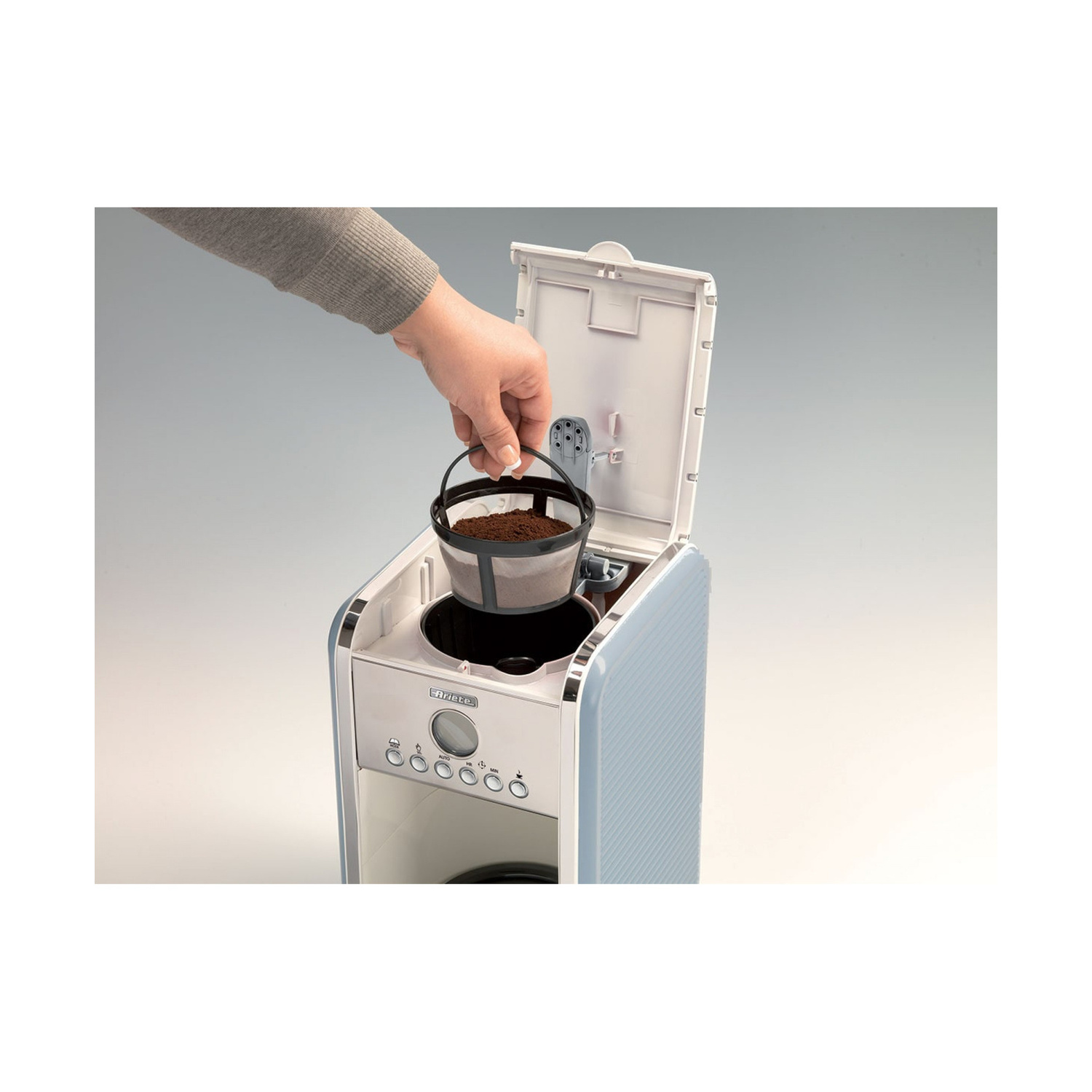Una mano inserisce un filtro da caffè con il macinato in una caffettiera azzurra.