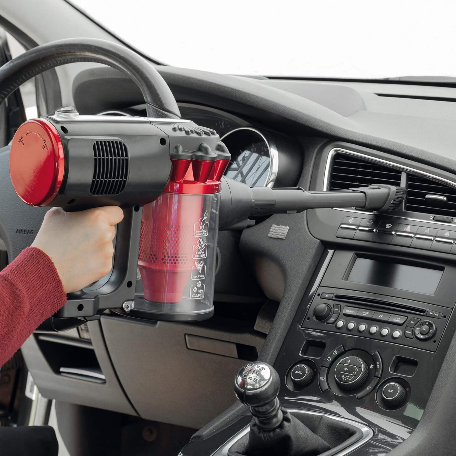 Una persona usa un piccolo aspirapolvere portatile rosso per pulire le bocchette d'aria dell'auto.