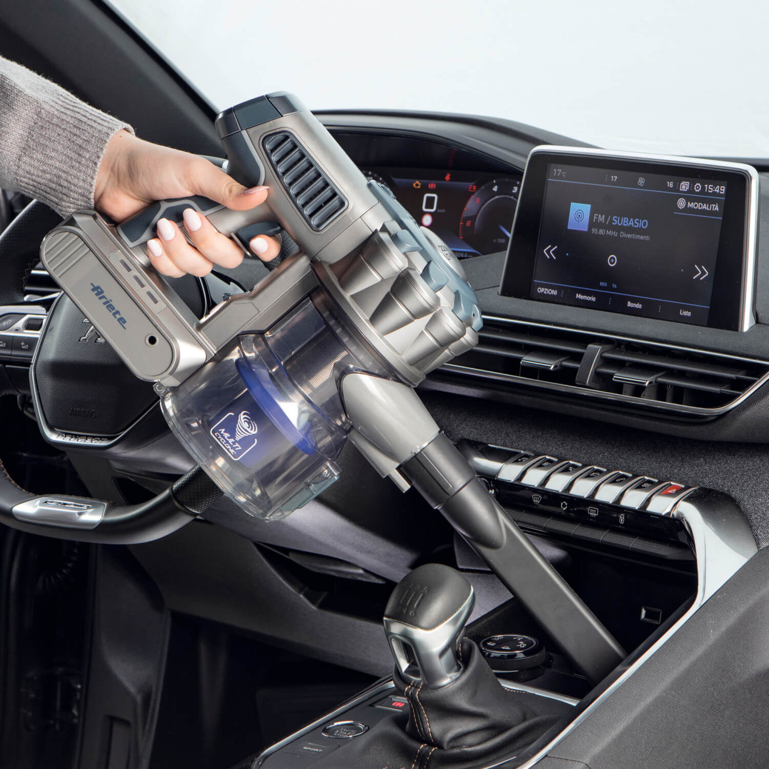 Una persona usa un aspirapolvere portatile grigio per pulire la console centrale di un'auto.