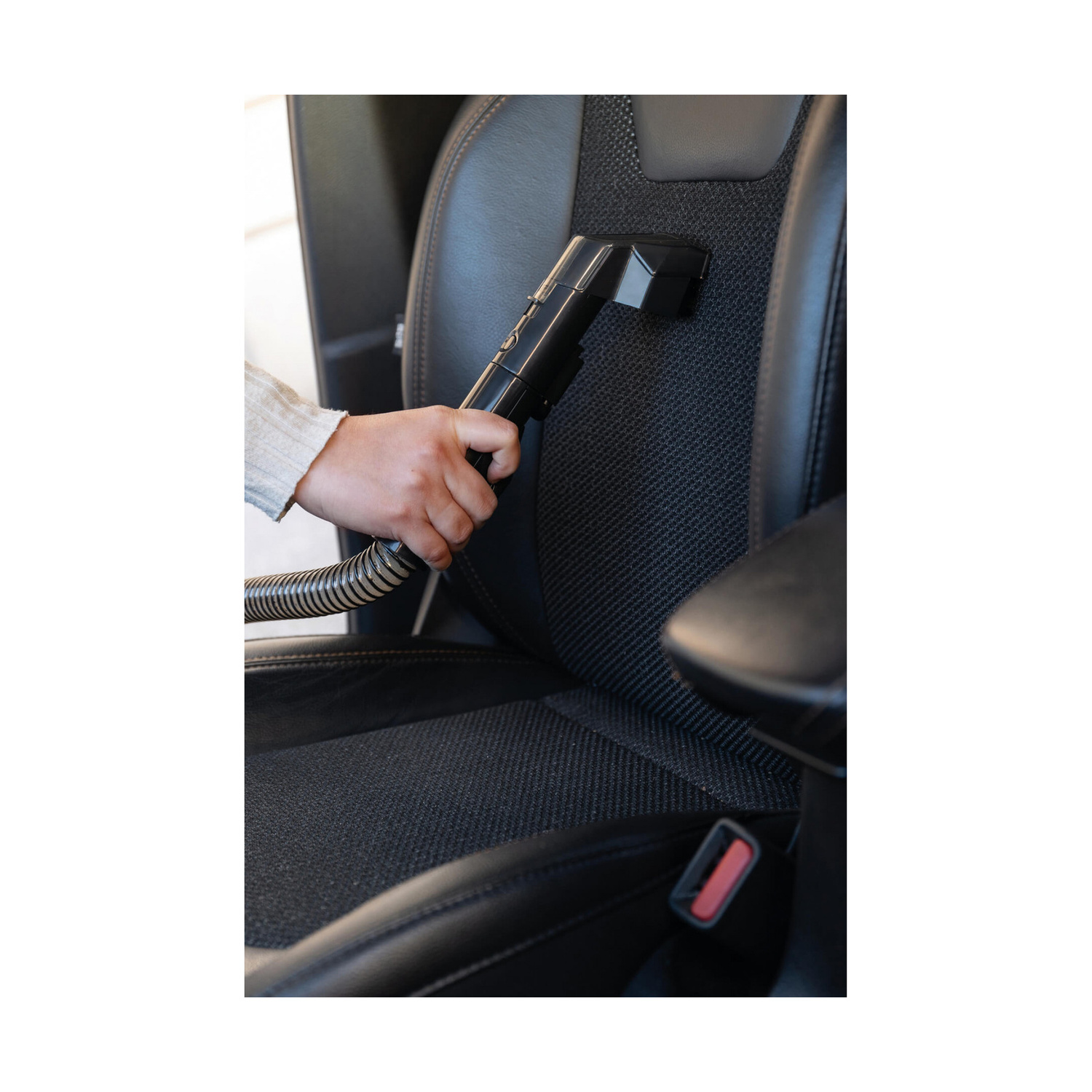 Una mano passa l'aspirapolvere su un sedile auto nero con un piccolo accessorio.