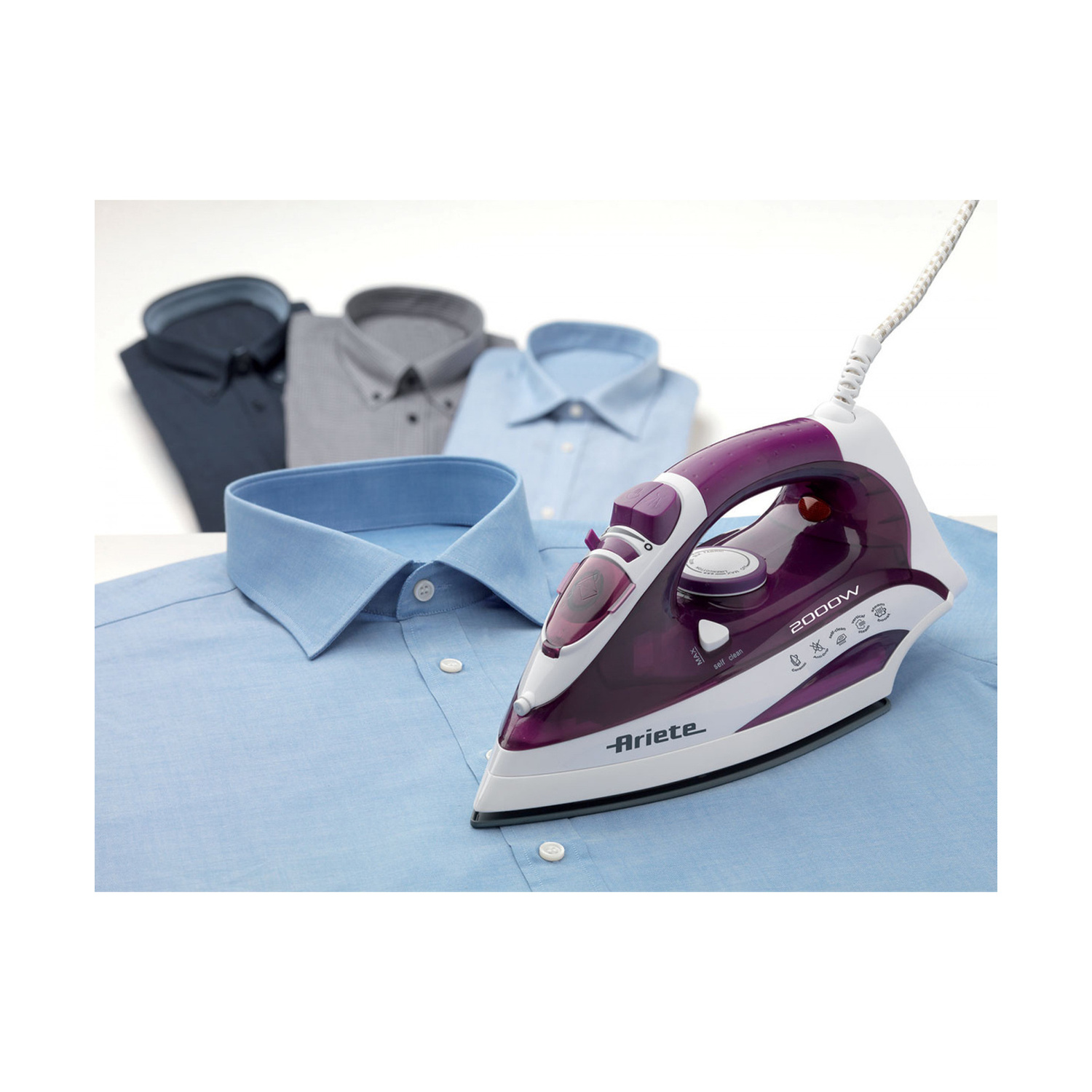 Un ferro da stiro Ariete viola e bianco poggia su una camicia azzurra, con tre camicie piegate sullo sfondo.