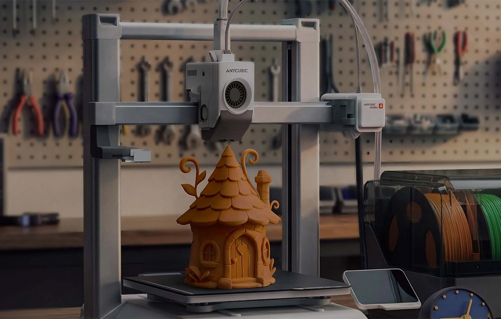 Egy 3D nyomtató egy kis barna tündérházat nyomtat egy műhelyben, háttérben szerszámokkal.