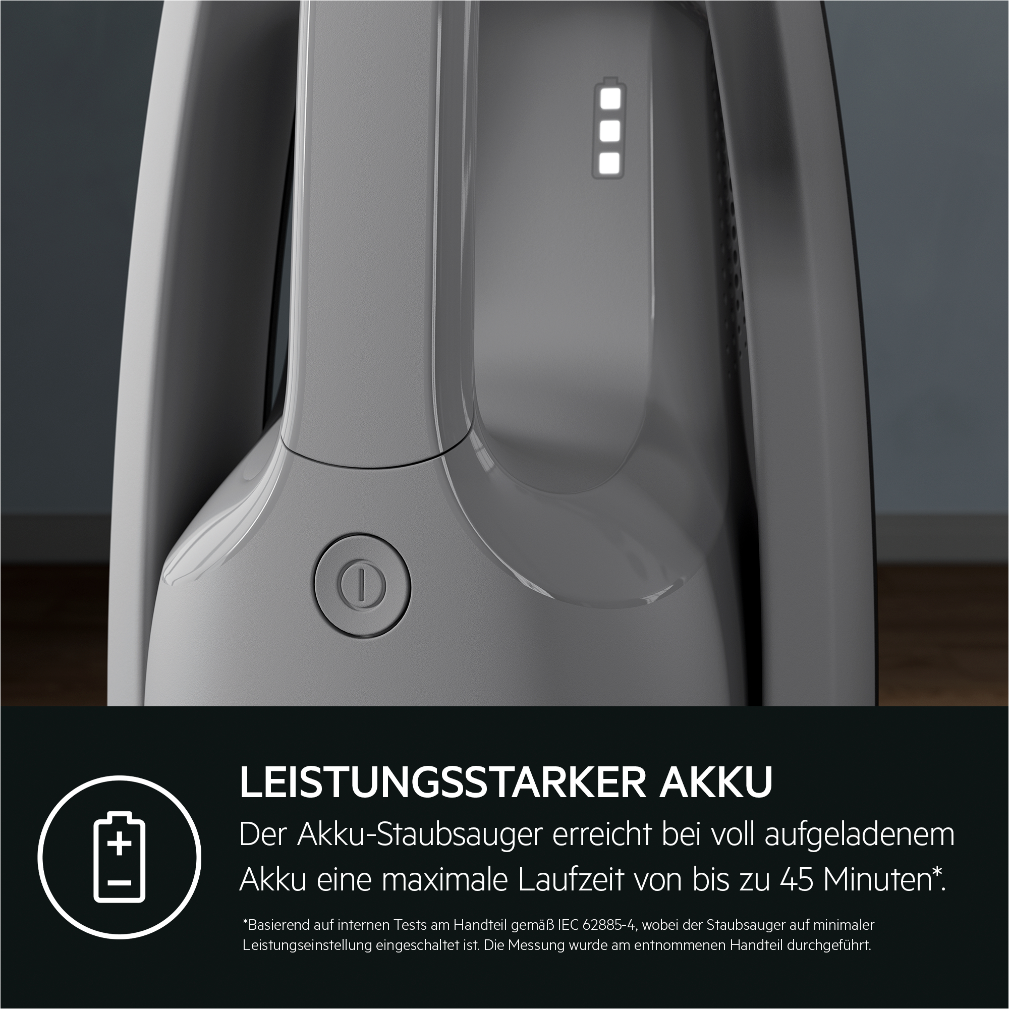 Grauer Akku-Staubsauger mit Ein-Aus-Schalter und leuchtender Batterieanzeige, unten Text und Akku-Symbol.