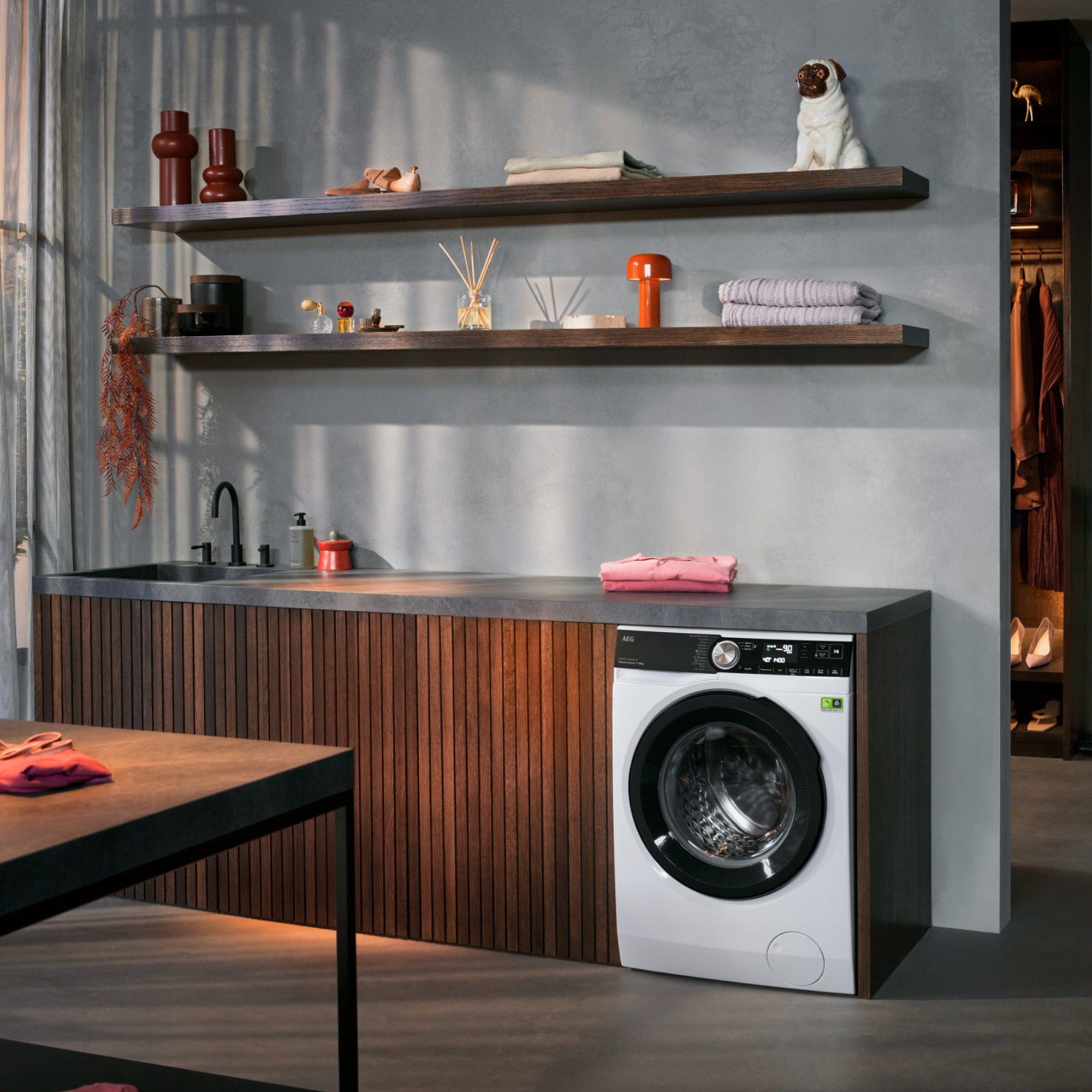 Moderne Waschküche mit Holzelementen, Regalen und einer weißen Waschmaschine unter der grauen Arbeitsplatte.
