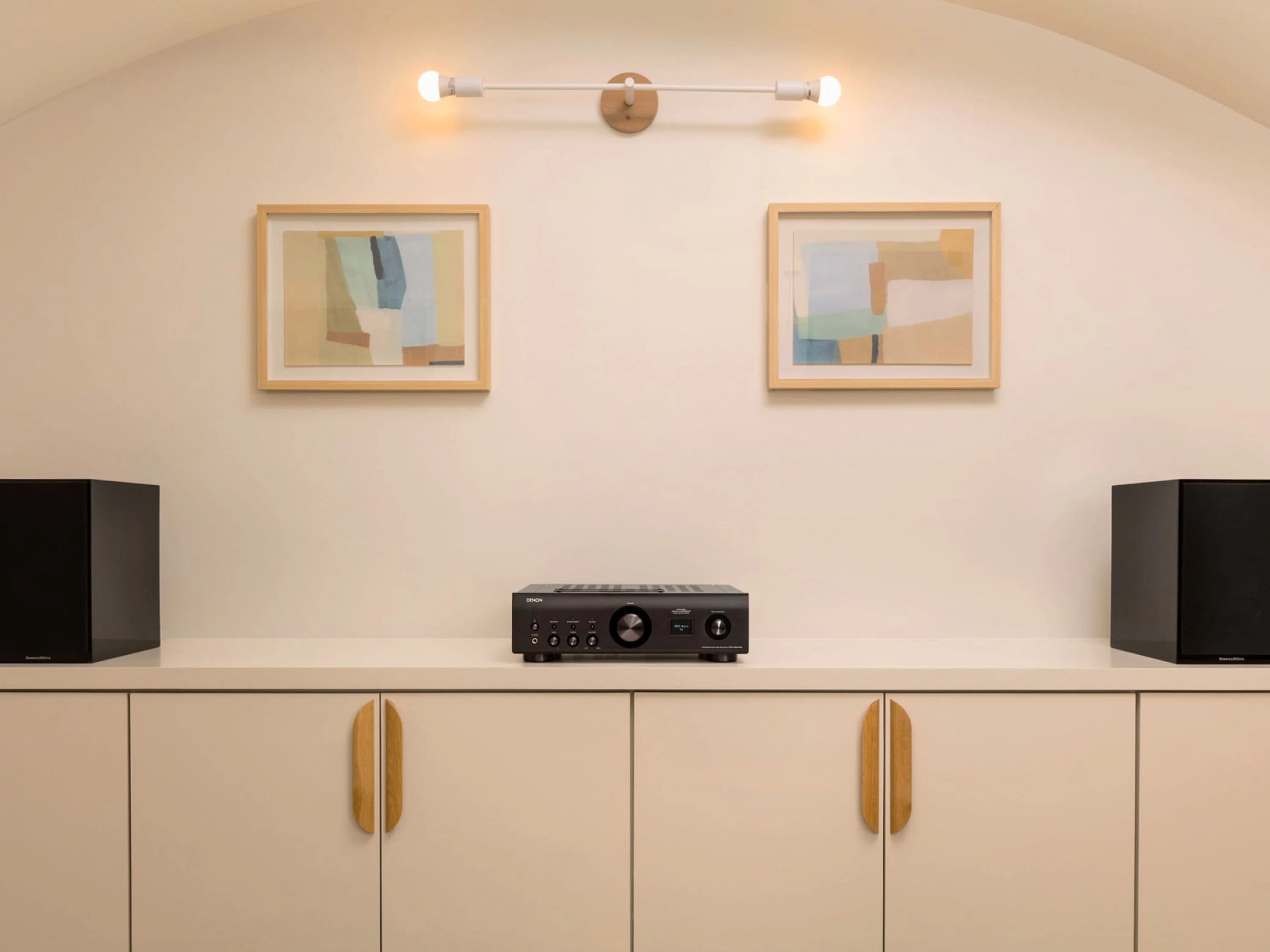 Ein Audiosystem steht auf einer weißen Kommode, flankiert von zwei gerahmten abstrakten Gemälden und beleuchtet von Lampen.