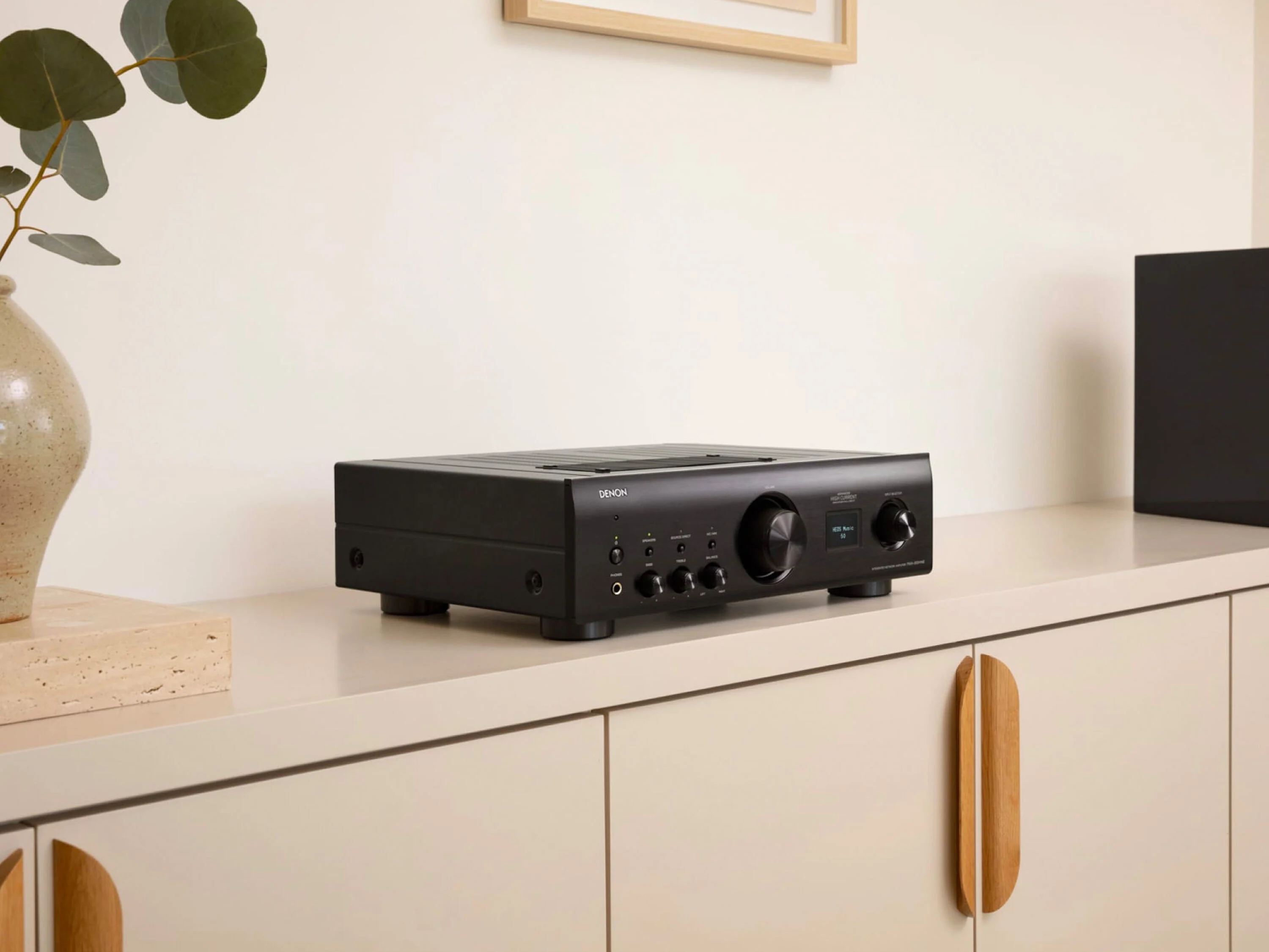 Ein schwarzer Denon Verstärker steht auf einem hellen Schrank in einem minimalistischen Raum.