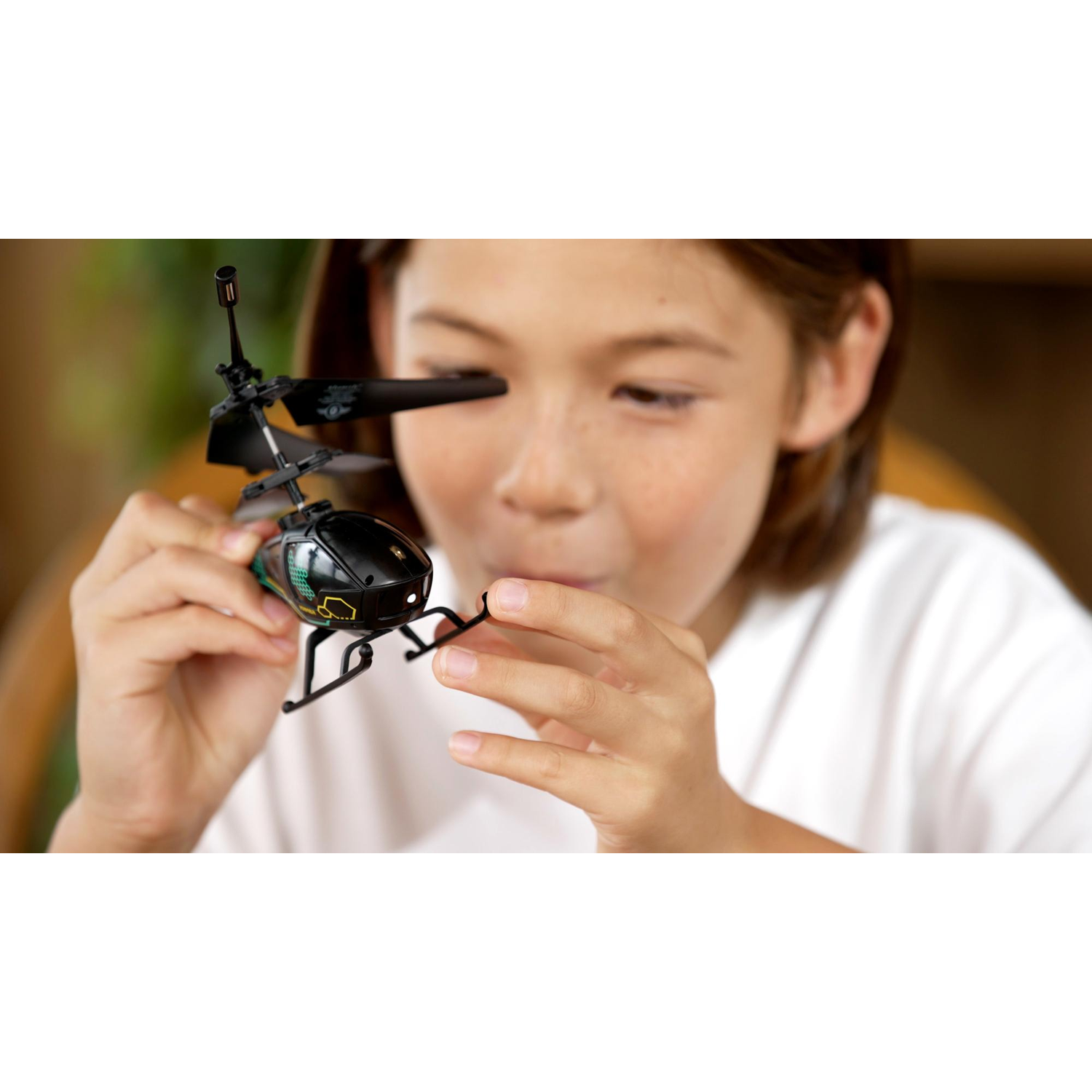 A child holds a small black toy helicopter, looking at it with curiosity.