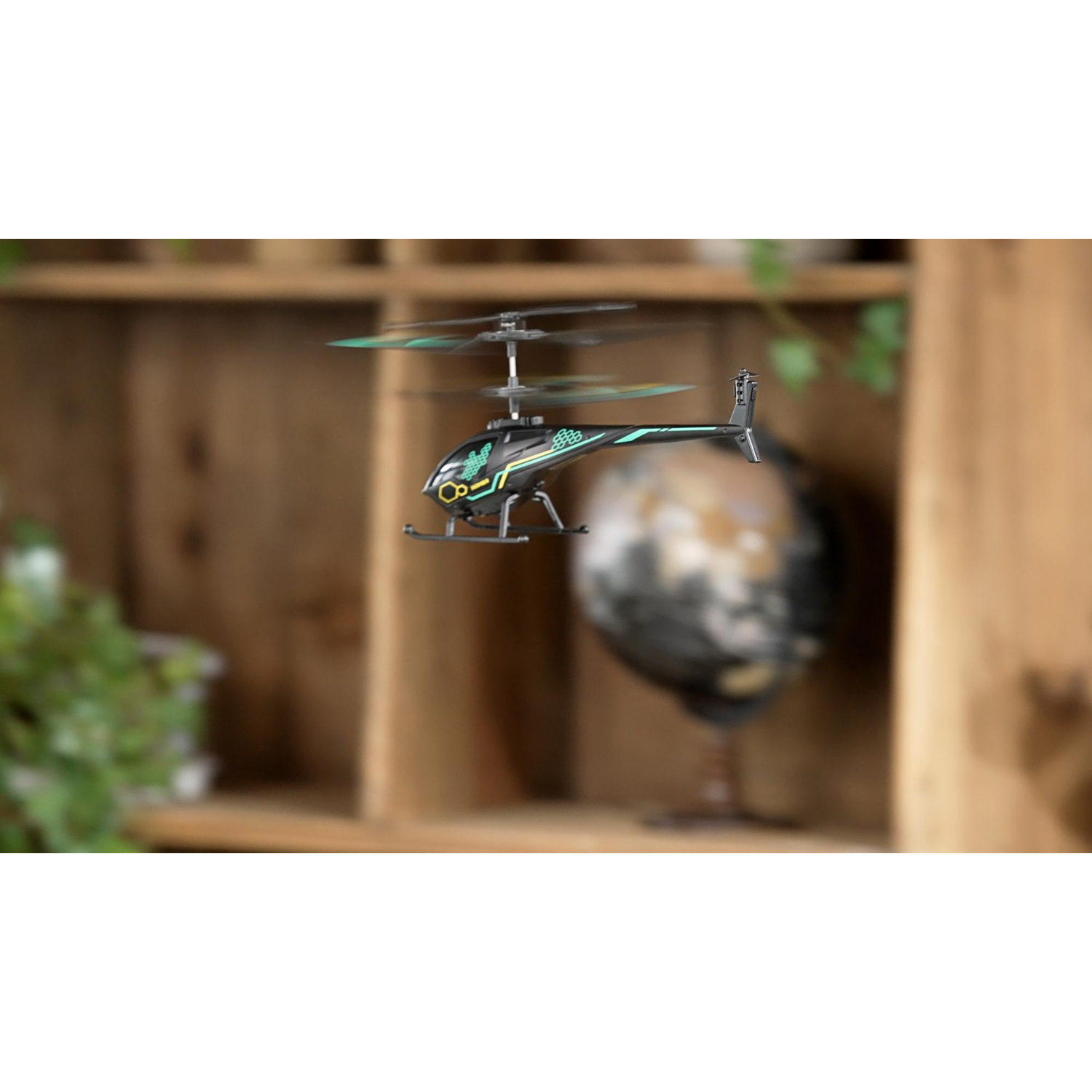 A black RC helicopter hovers indoors, with blurred wooden shelves and a globe in the background.