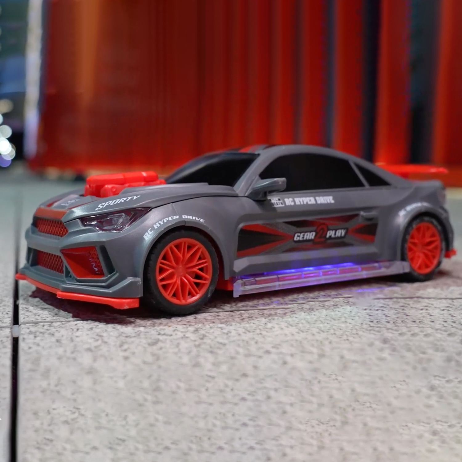 Grey toy car with red wheels and accents parked on a grey floor.