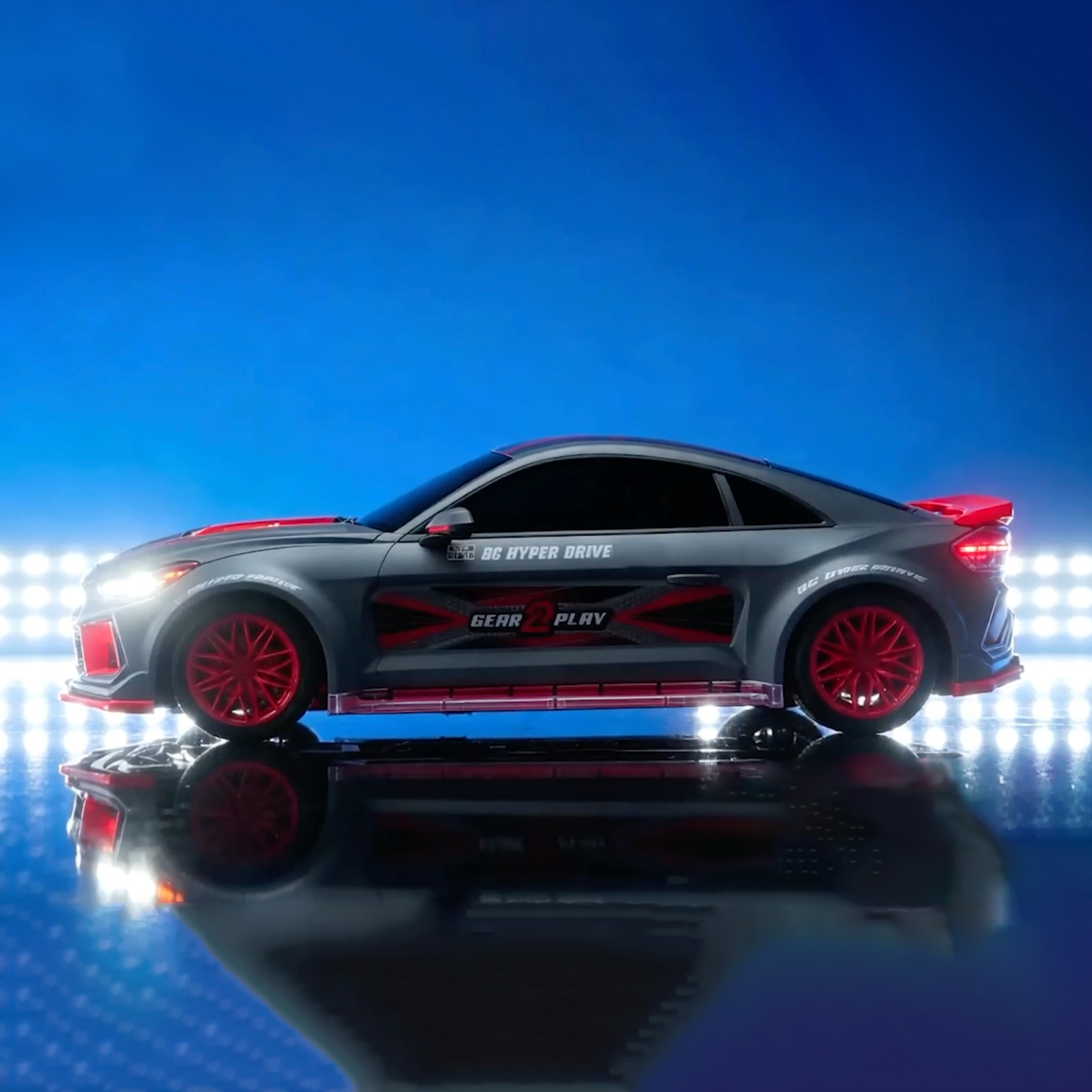 Gray remote control car with red rims and text, parked on a reflective surface against a blue background.