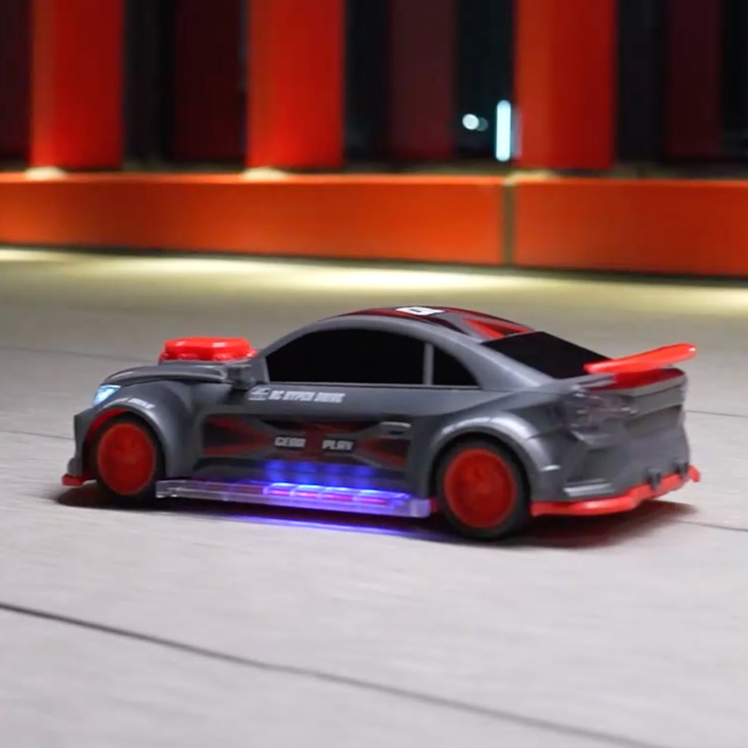 A grey RC car with red wheels and blue underglow lights on a smooth surface against a red background.