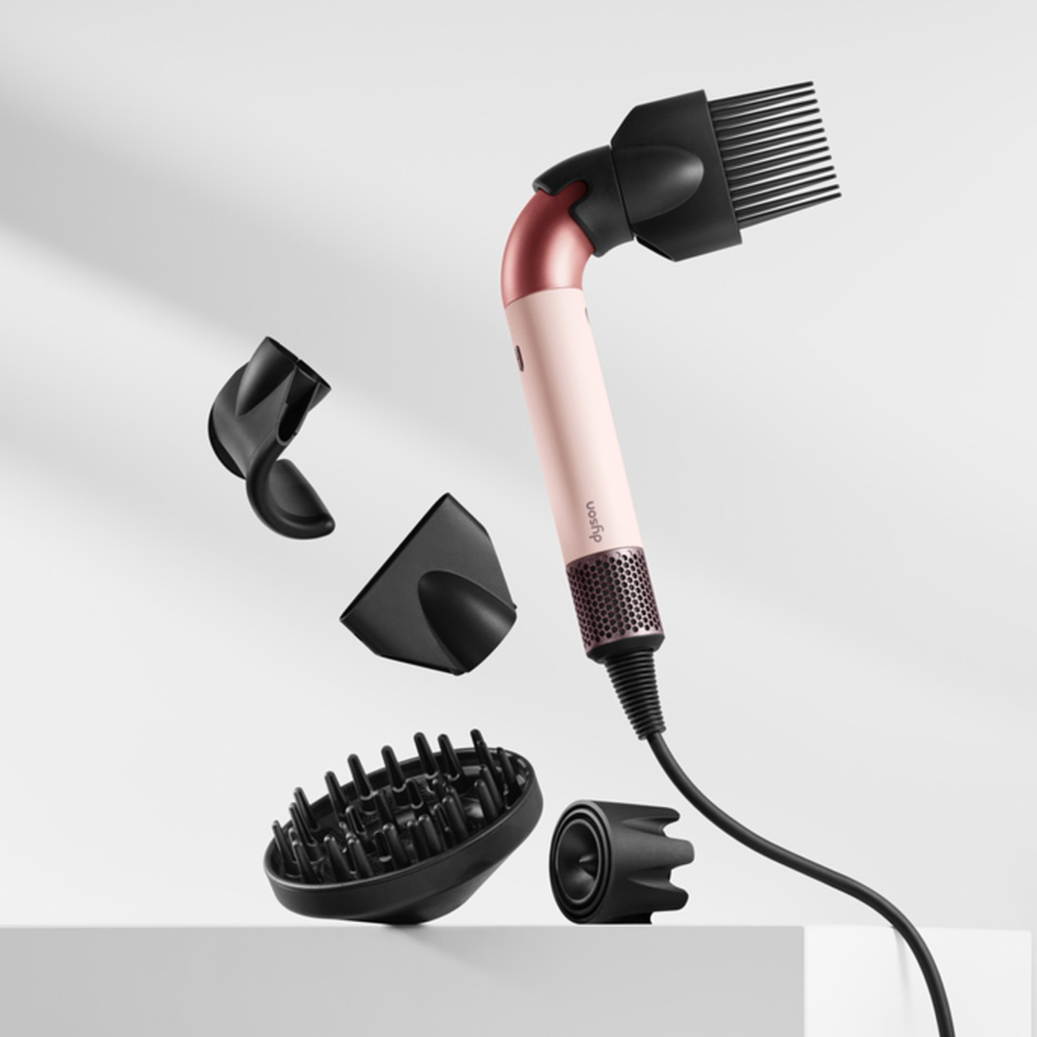 A pink and black hair dryer with four attachments floating around it on a white surface.