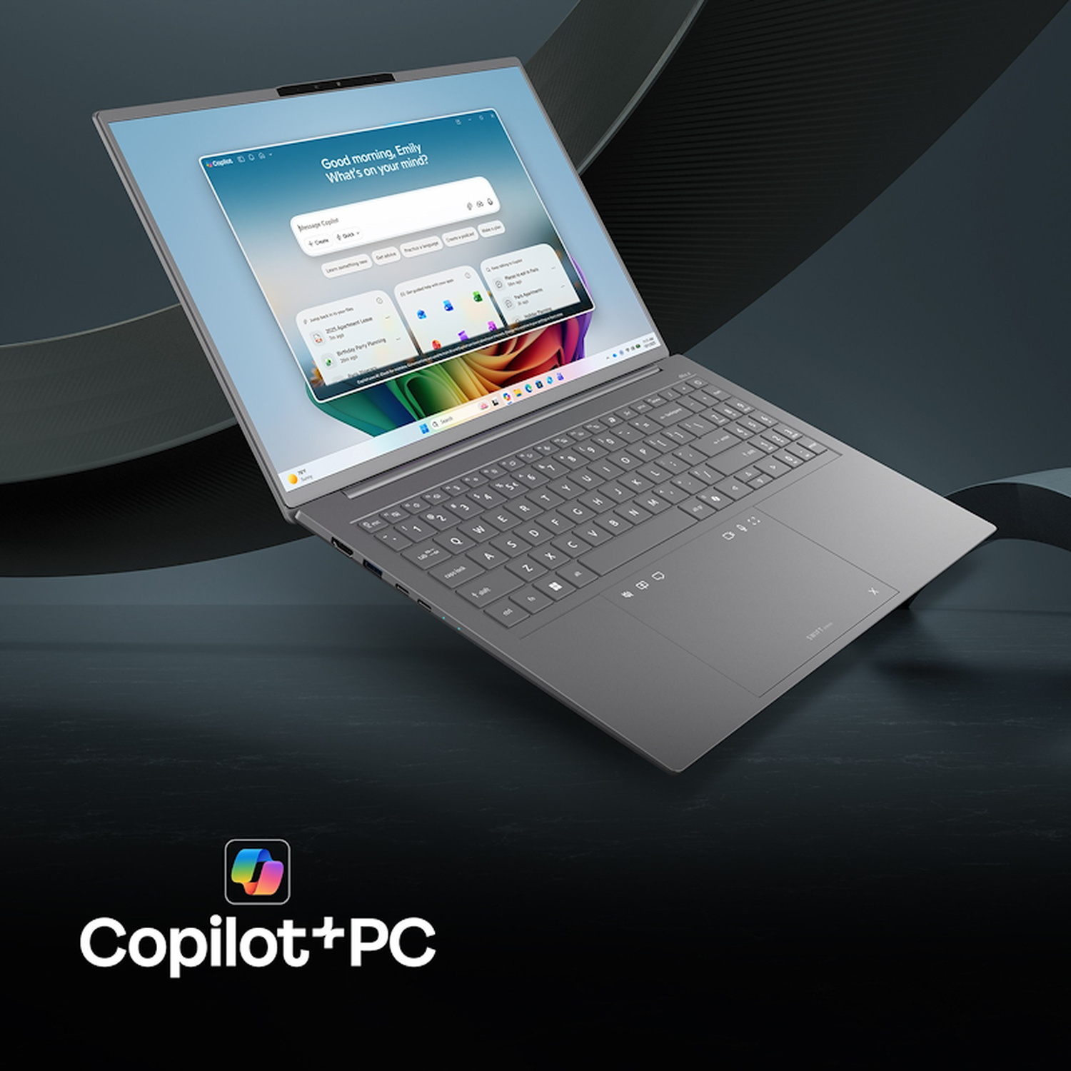 Un laptop grigio Copilot+ PC su superficie scura, con il logo Copilot in basso a sinistra.