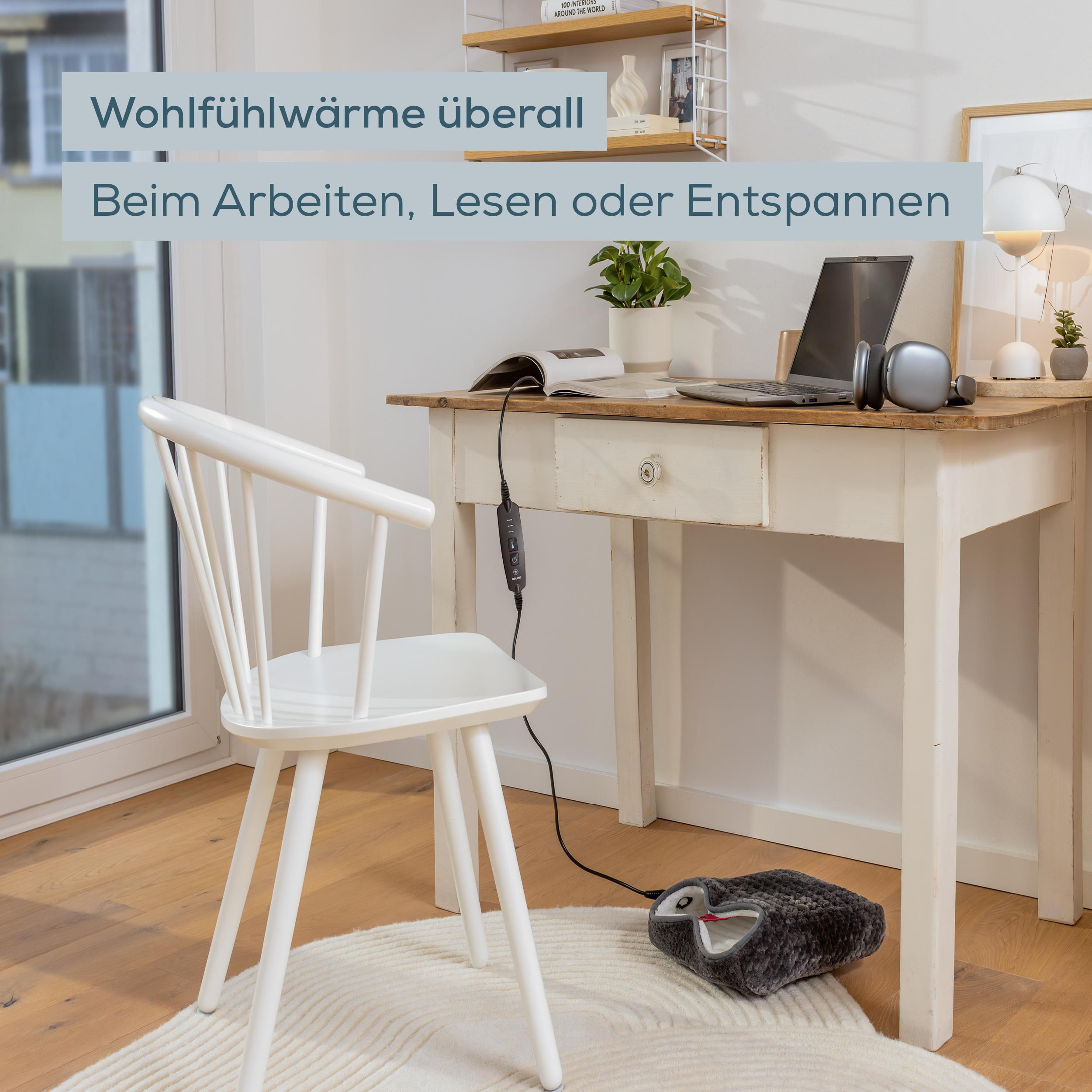Ein heller Arbeitsplatz mit Laptop, weißem Stuhl und einem grauen Fußwärmer auf einem Teppich.