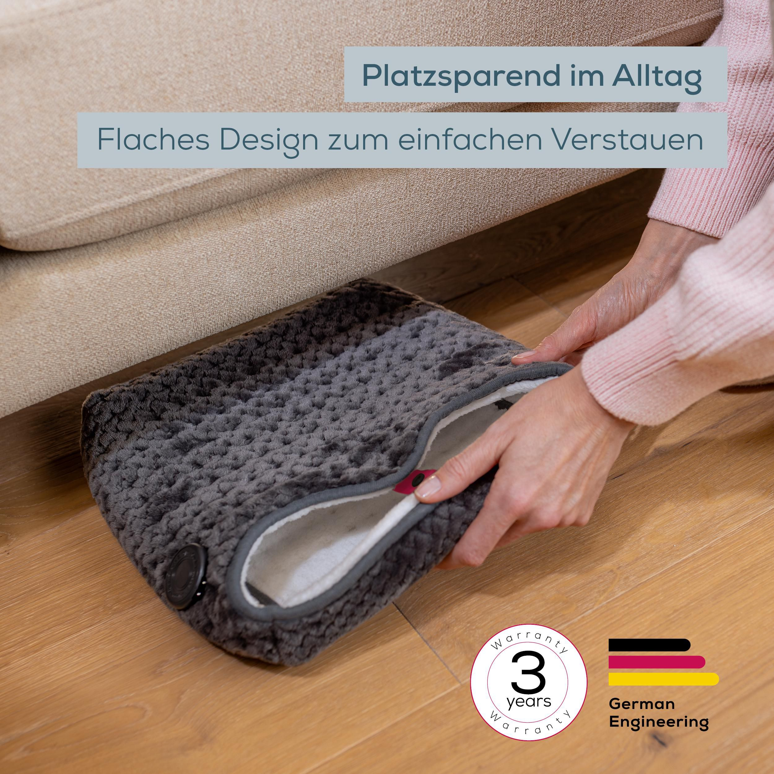 Person verstaut ein graues, flaches Wärmekissen unter dem Sofa.