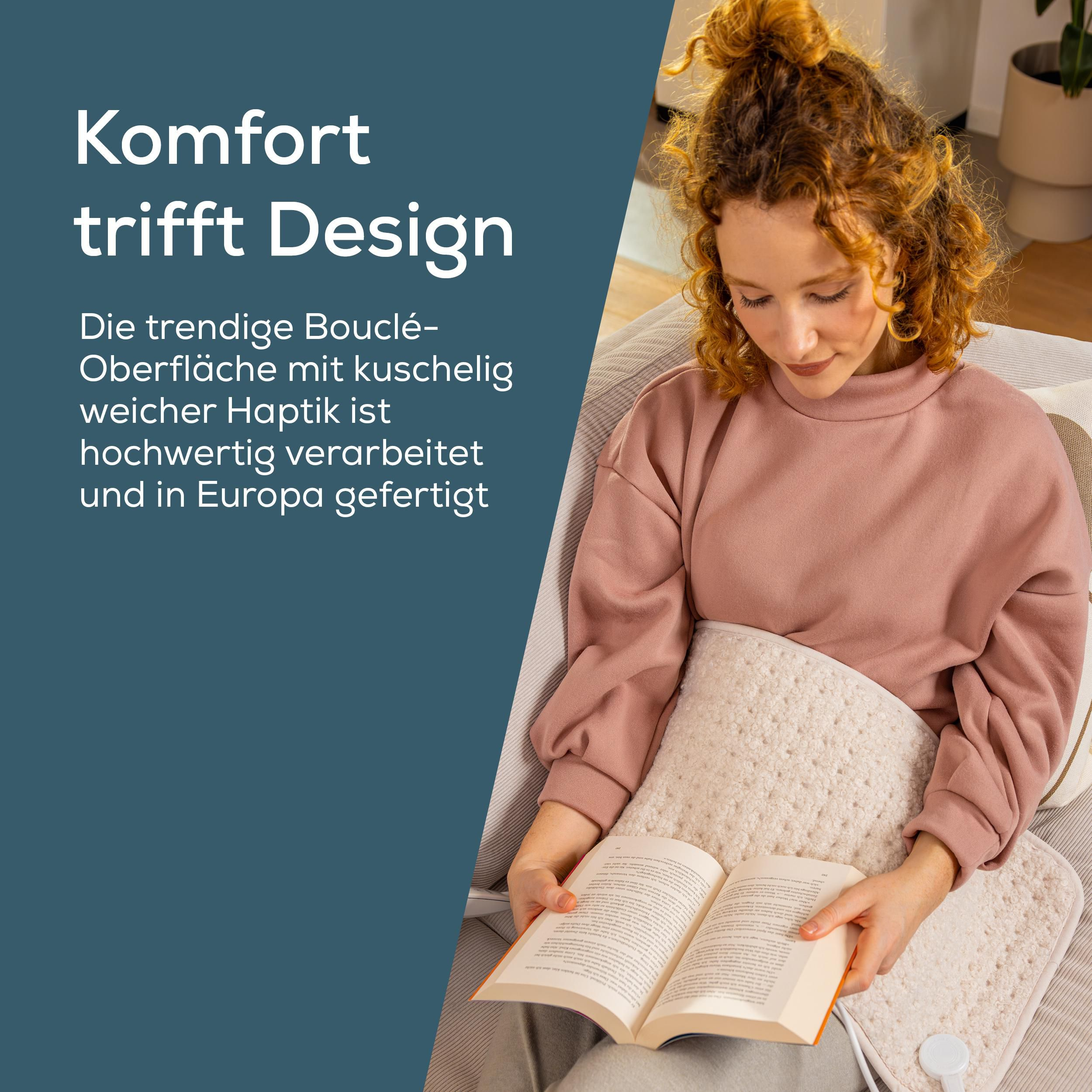 Eine rothaarige Frau sitzt auf einem Sofa, liest ein Buch und hat eine flauschige Heizweste auf dem Schoß.