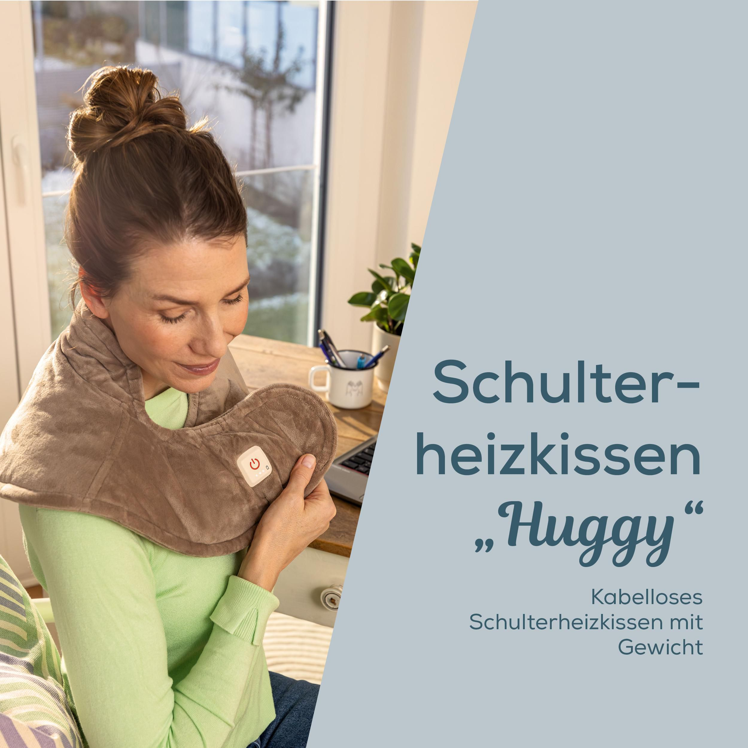 Eine Frau trägt ein graues Schulterheizkissen "Huggy" in einem hellen Raum.