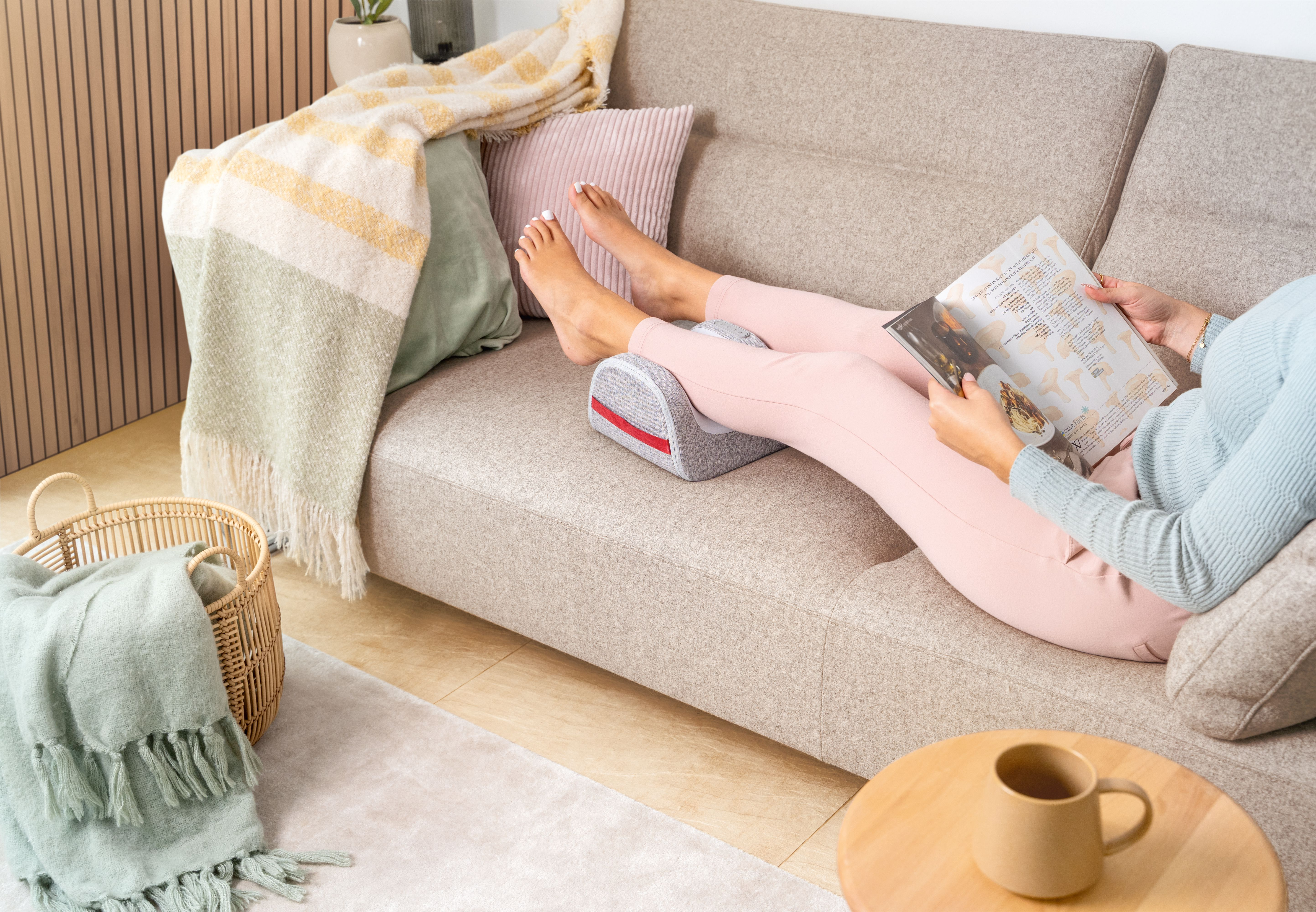 Frau entspannt auf einem Sofa, liest ein Magazin und lagert ihre Beine auf einem grauen Kissen hoch.