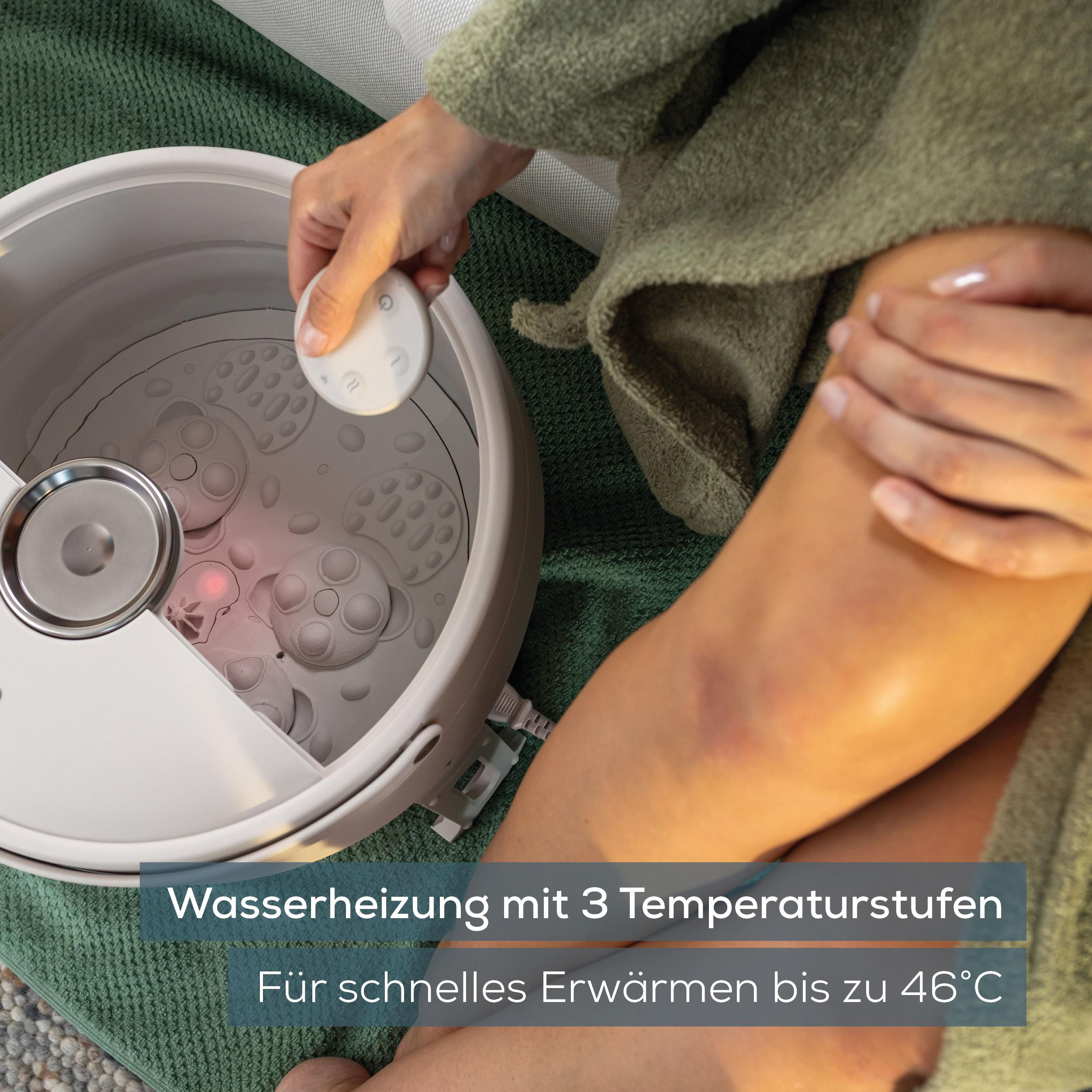 Person hält eine Fernbedienung über ein weißes Fußsprudelbad auf einem grünen Teppich.
