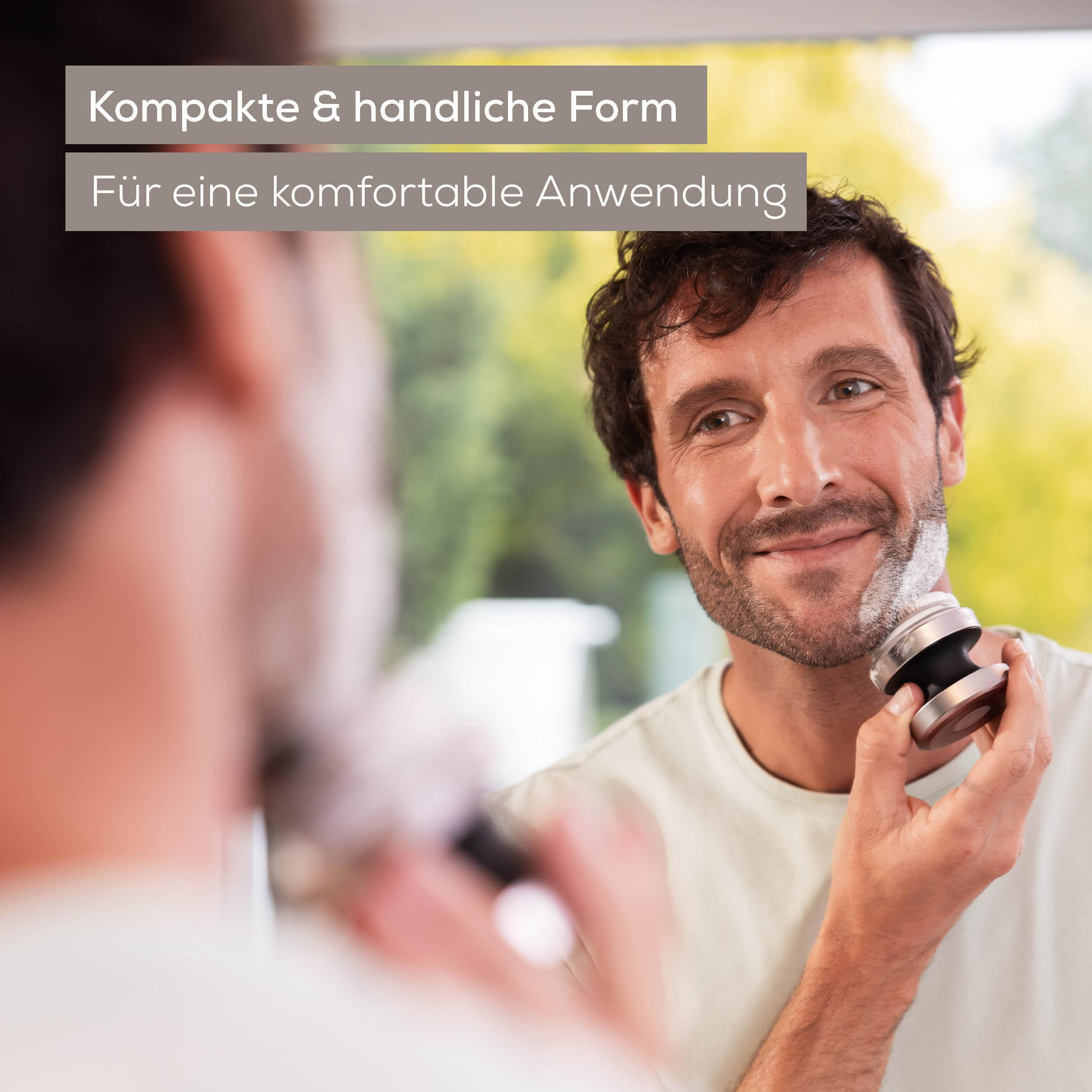 Ein lächelnder Mann rasiert sich vor dem Spiegel mit einem kleinen Elektrorasierer.