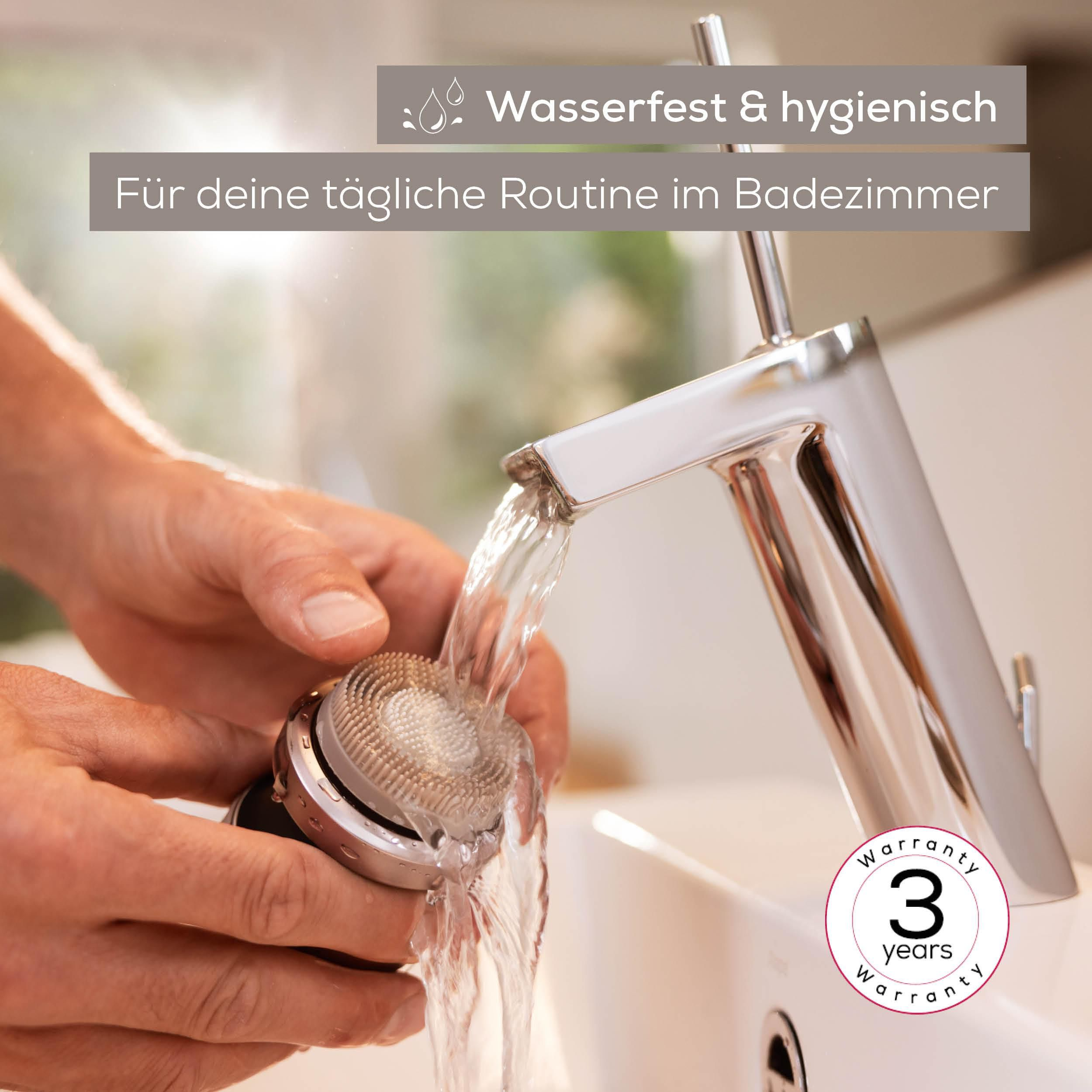 Hände halten eine Gesichtsbürste unter fließendem Wasser aus einem modernen Wasserhahn.