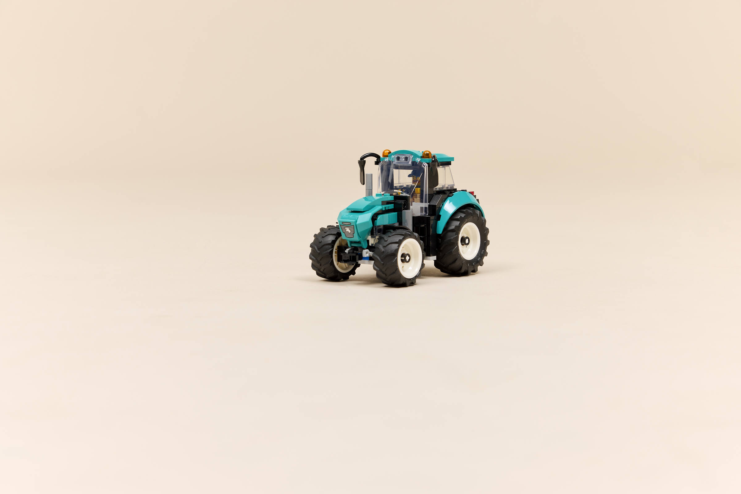 Un tracteur jouet turquoise en blocs de construction sur fond beige.