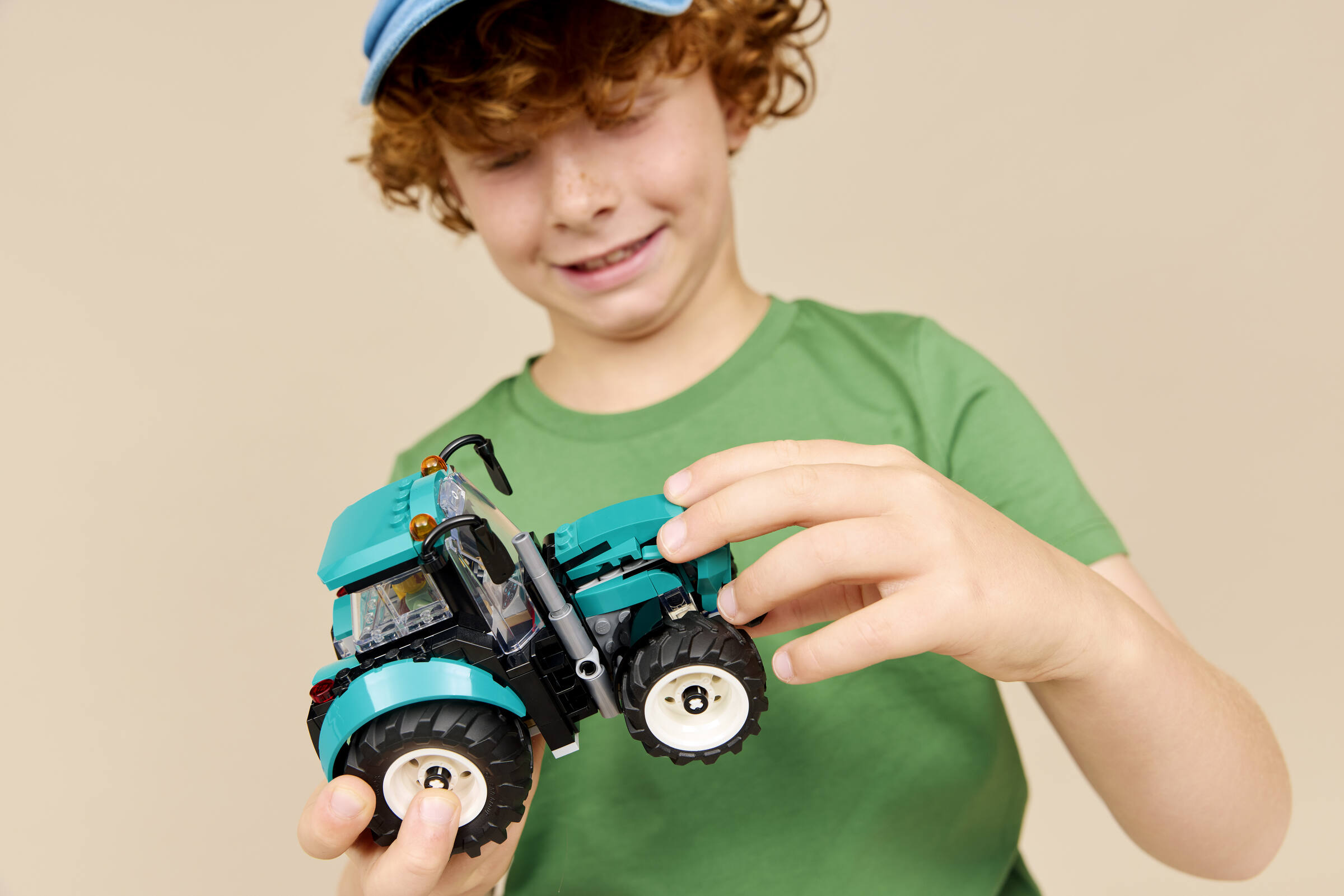 Garçon aux cheveux roux portant un t-shirt vert assemblant un tracteur jouet bleu.