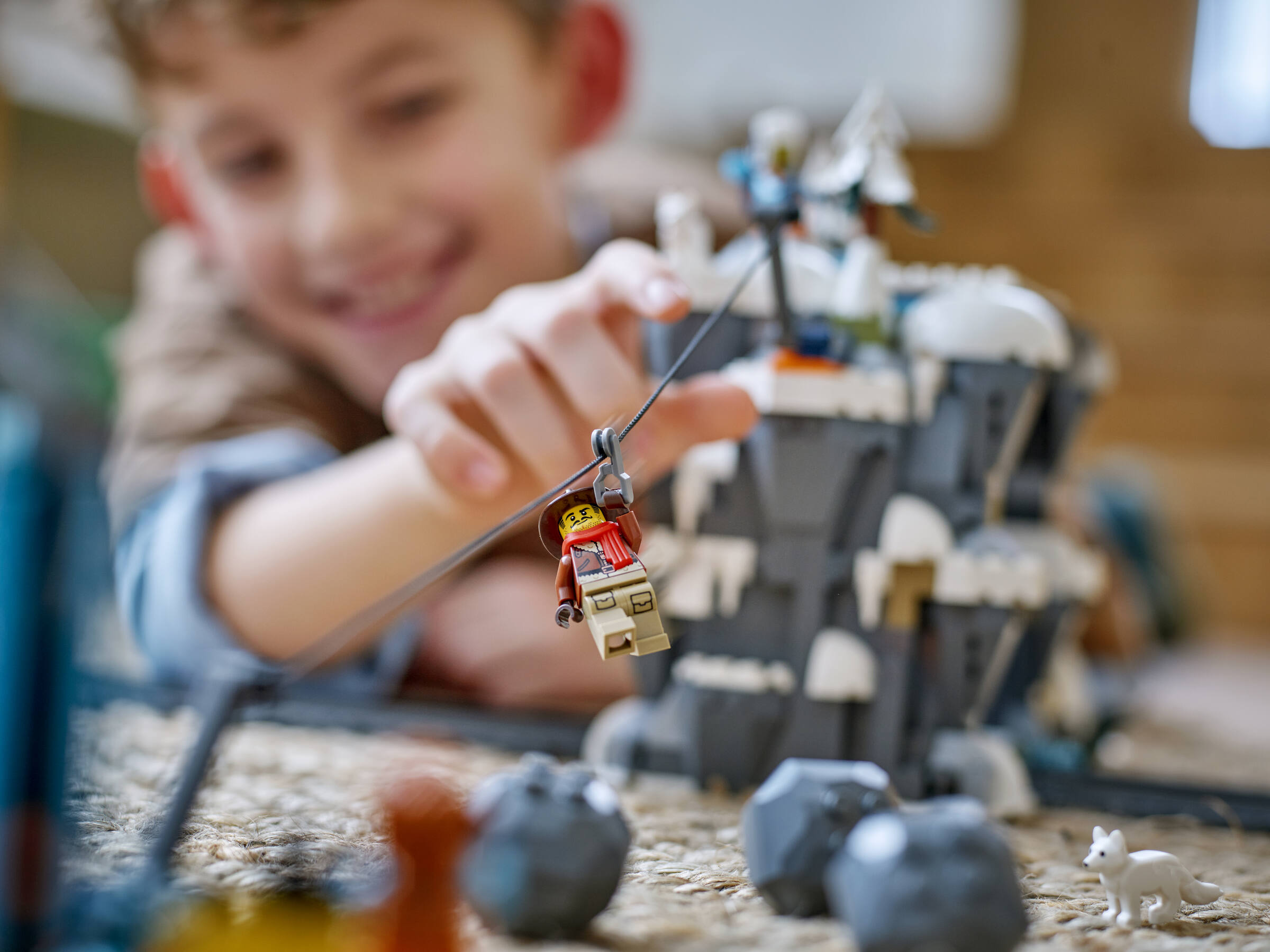 Un garçon heureux joue avec un set Lego, faisant glisser une figurine sur une tyrolienne devant un décor de montagne.