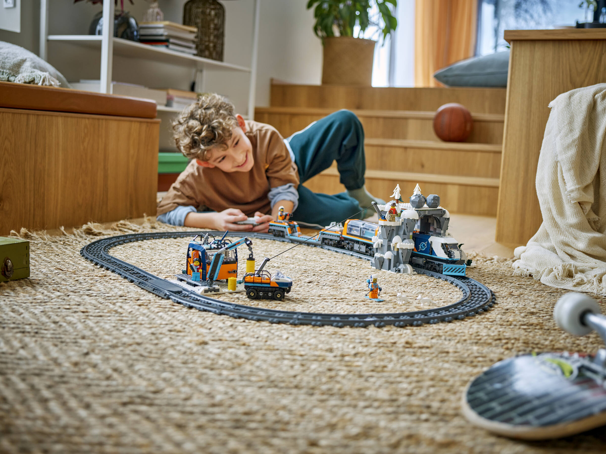 Un garçon est étendu sur un tapis et joue avec un train Lego et une station de neige.