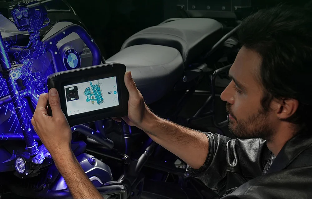 Egy férfi tabletet használ, hogy kék hologram grafikákat nézzen egy motorkerékpáron.