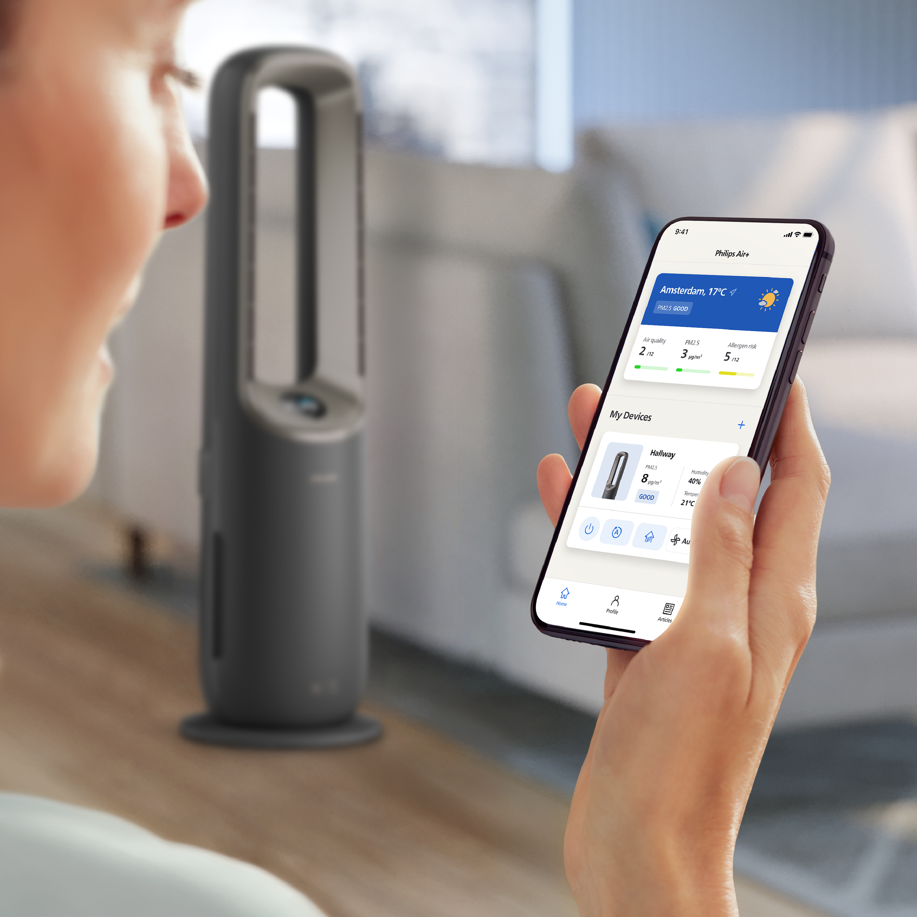 Person hält ein Smartphone, das eine App zur Steuerung eines grauen Luftreiniger-Turms anzeigt.