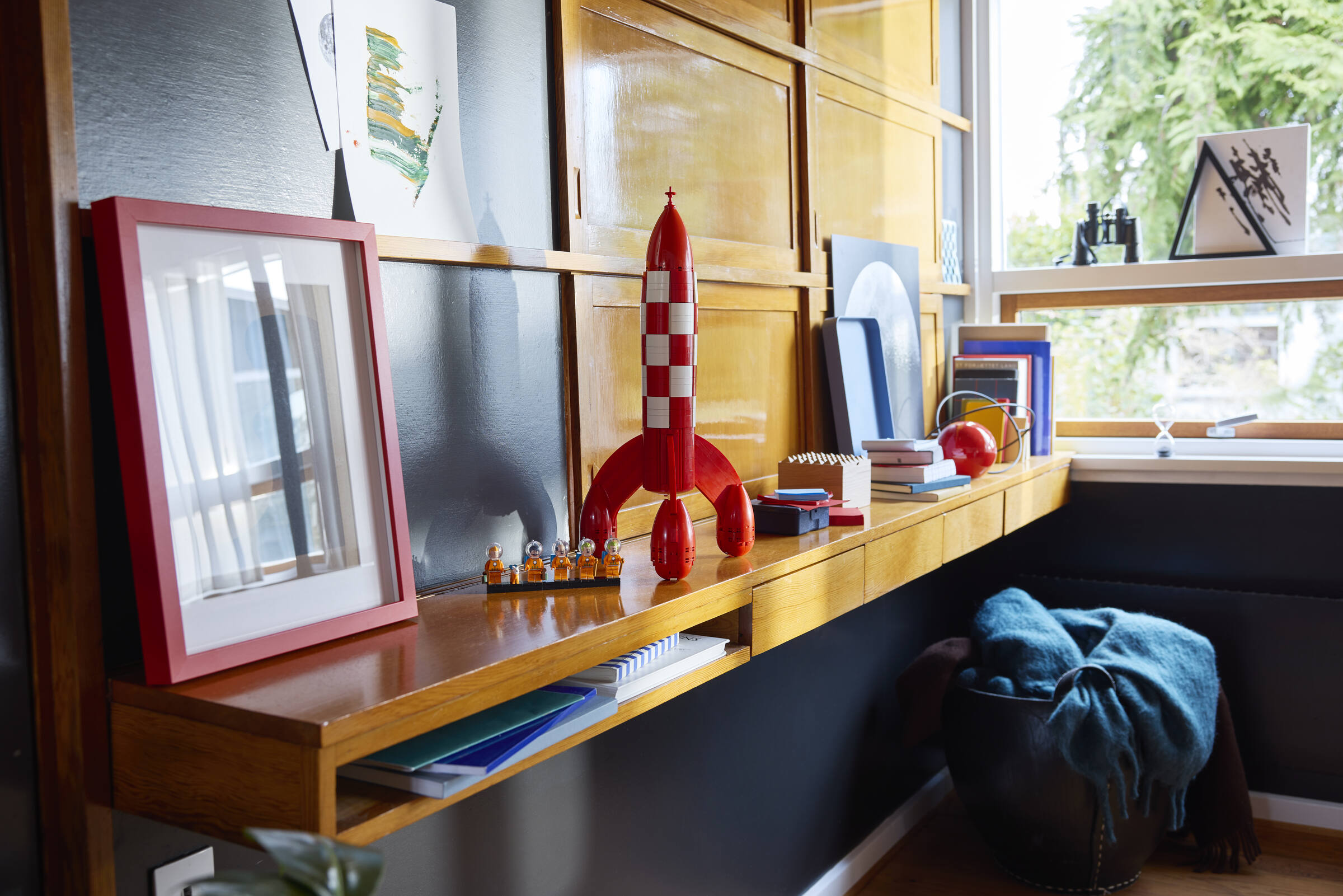 Un modèle de fusée rouge repose sur une étagère en bois à côté d'un cadre rouge et de petites figurines.