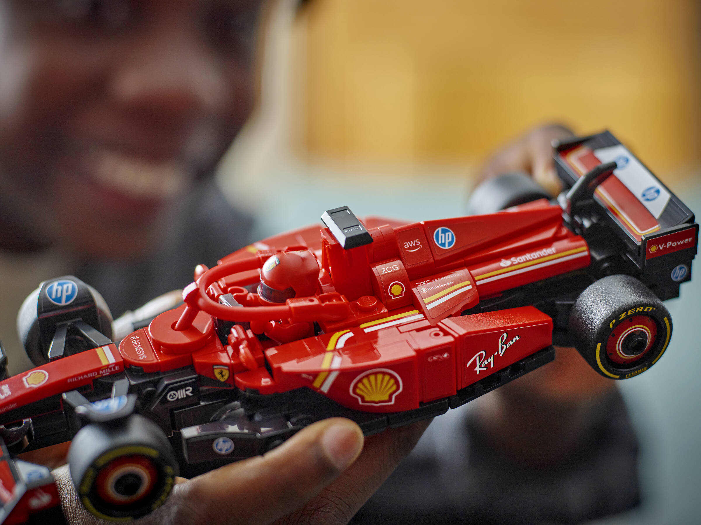 Eine Person hält ein rotes Lego-Formel-1-Auto mit Sponsor-Aufklebern in den Händen.