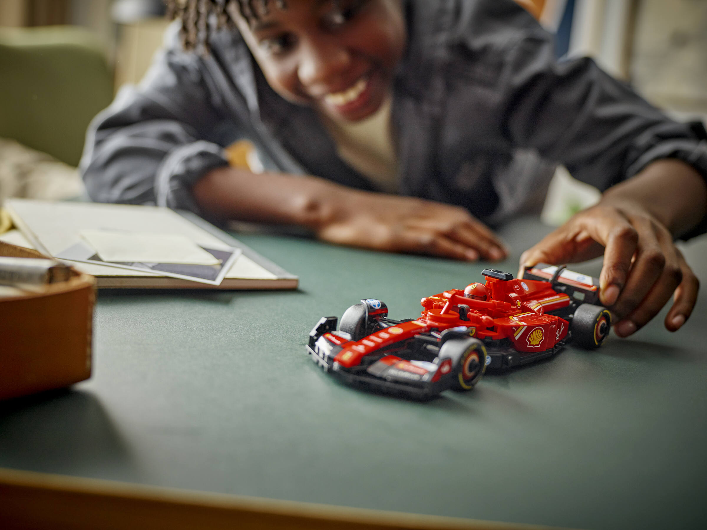 Ein Junge lächelt, während er ein rotes Formel-1-Spielzeugauto auf einem Tisch bewegt.