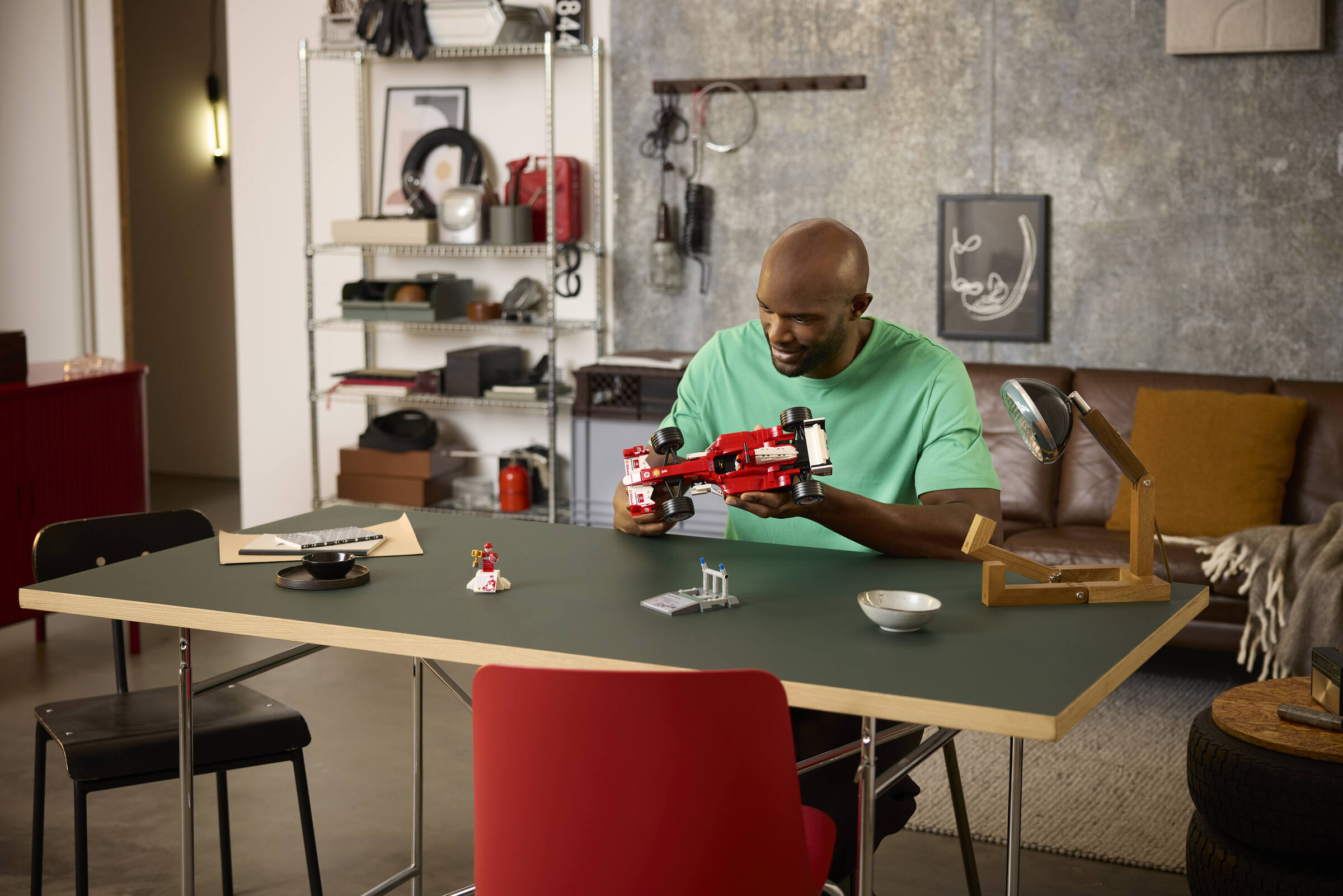Ein Mann im grünen Shirt baut am Tisch ein rotes LEGO-Formel-1-Auto auf.