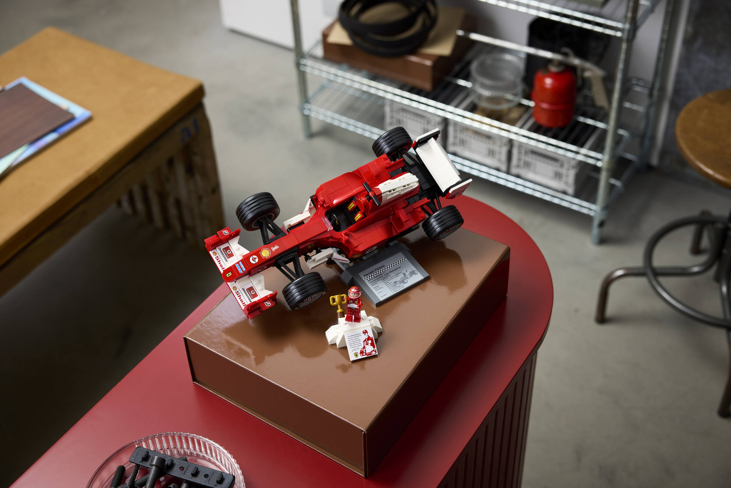 Ein rotes Lego Formel-1-Auto auf einer Box auf einem roten Tisch in einer Werkstatt.