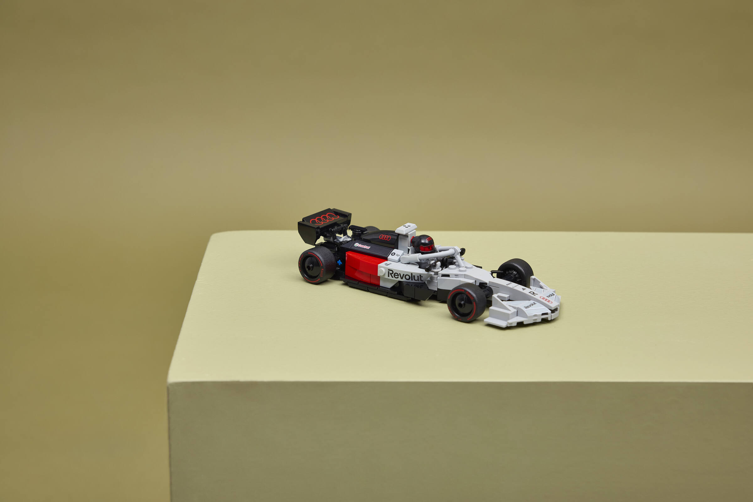 Ein weiß-schwarz-rotes Formel-1-Spielzeugauto steht auf einer hellgrünen Plattform vor einem passenden Hintergrund.