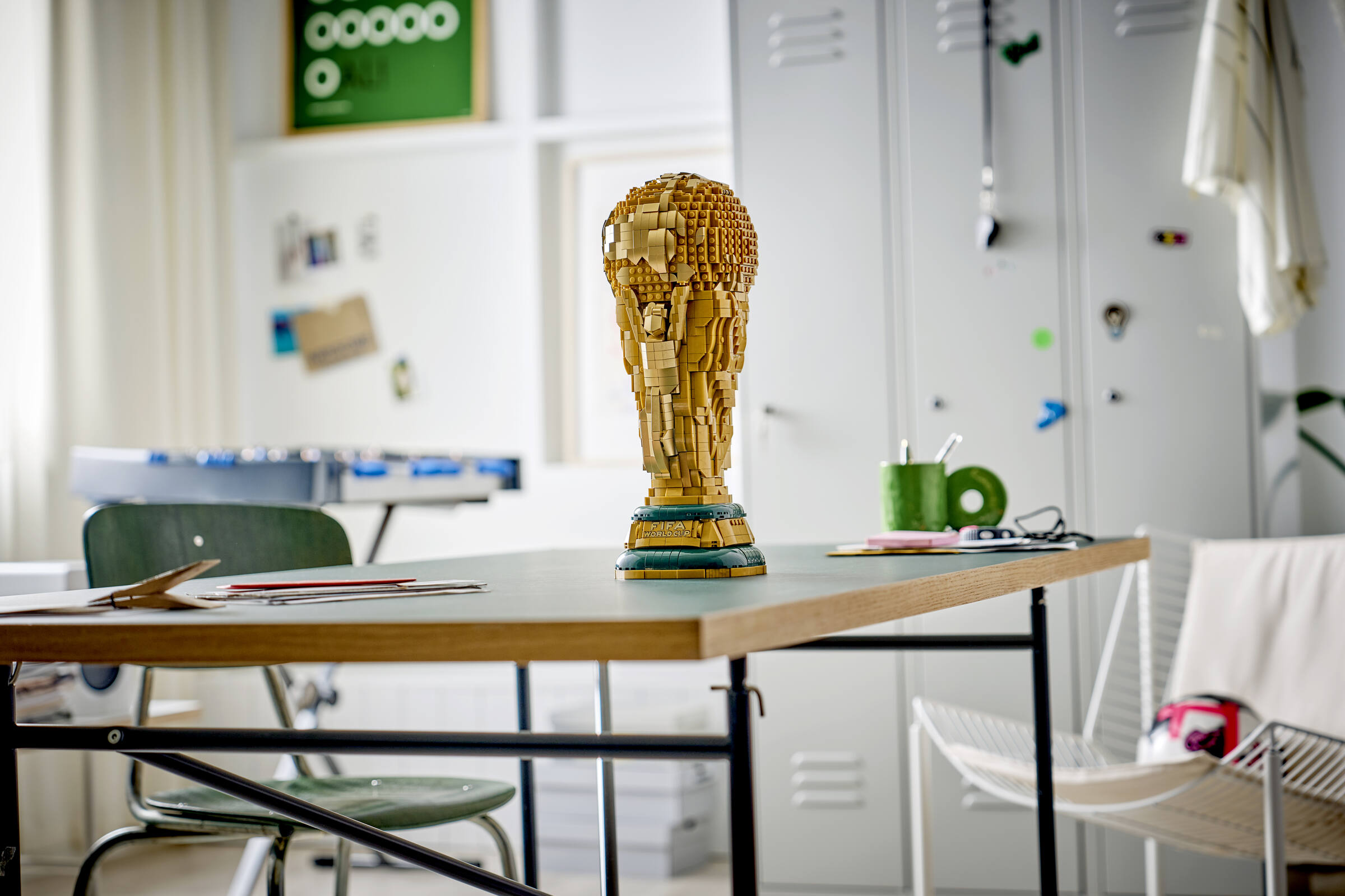 Ein detailgetreuer FIFA-Weltpokal aus Lego-Steinen steht im Vordergrund auf einem Schreibtisch in einem Raum.
