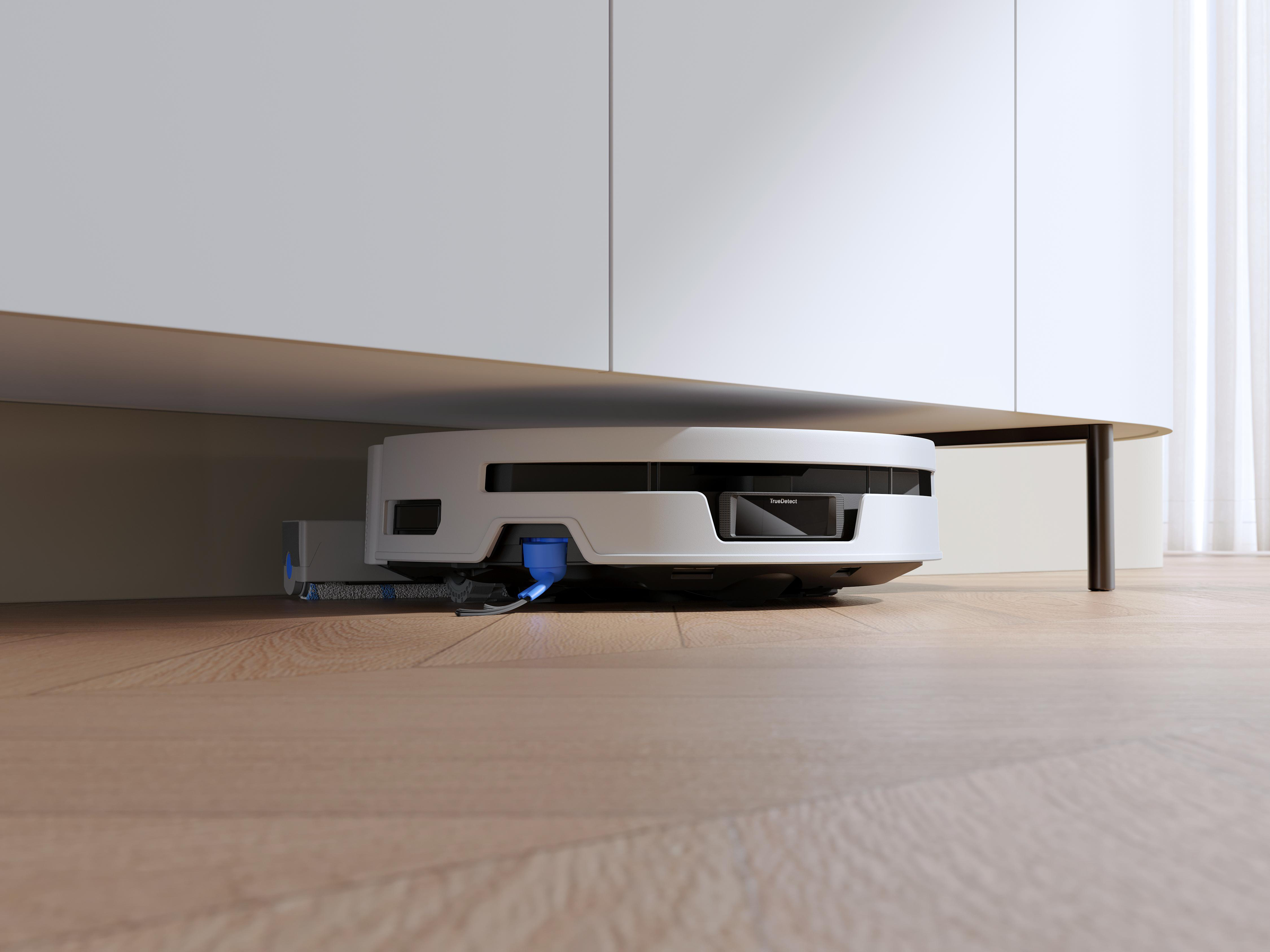 Ein weißer Roboterstaubsauger reinigt auf dem Holzboden unter einem weißen Schrank.