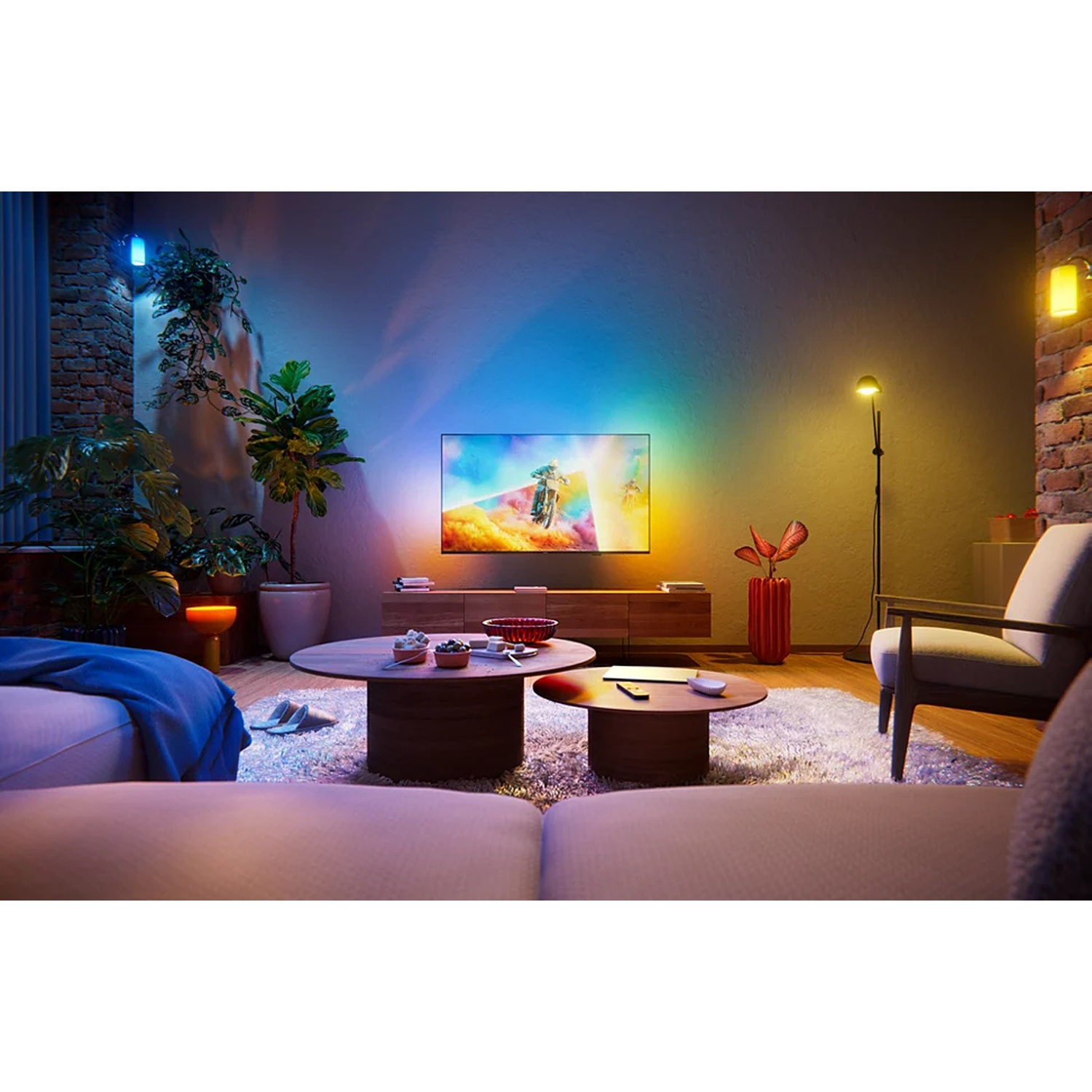 Salon confortable avec une télé éclairée projetant une lumière colorée sur le mur, des plantes et des tables basses.
