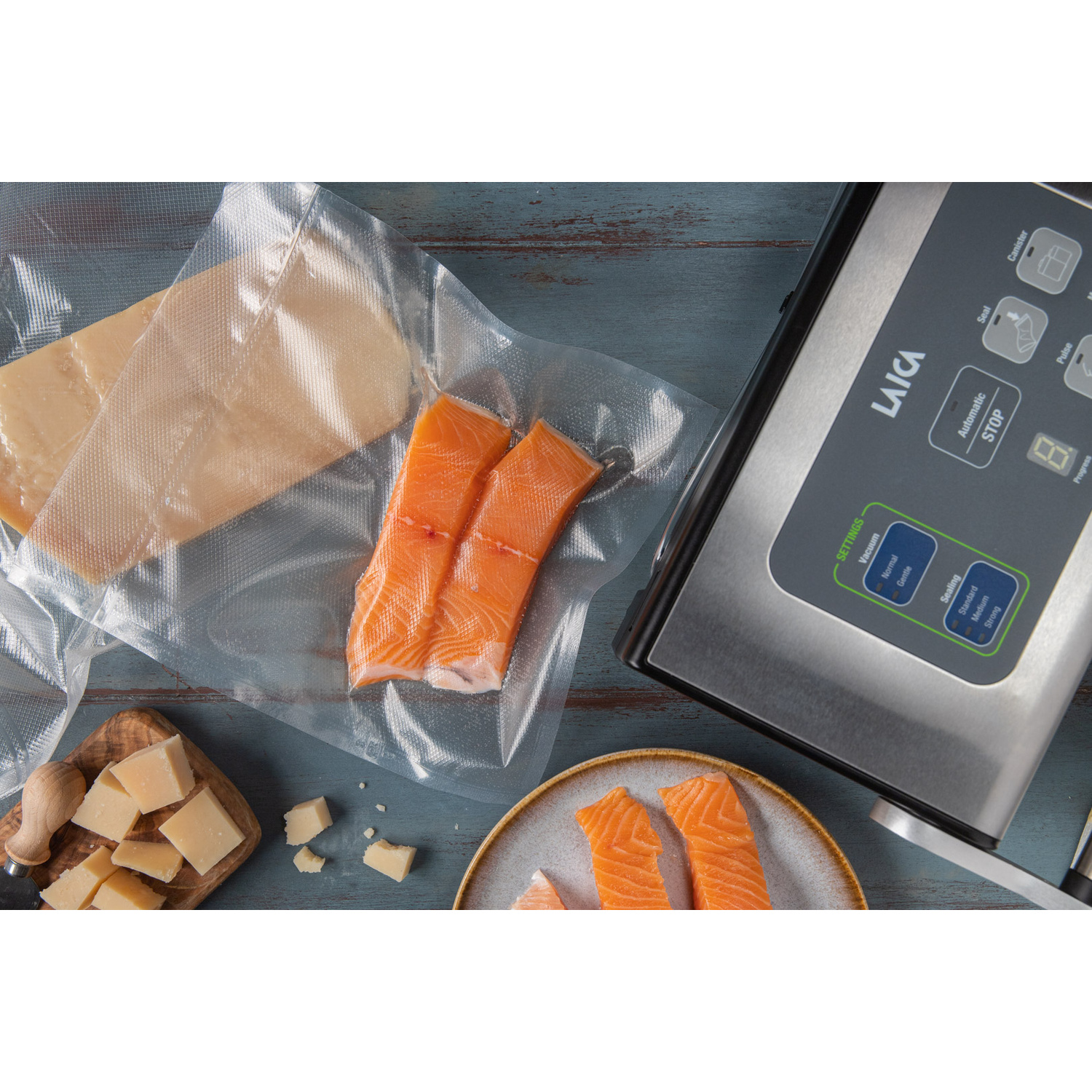 Una macchina sottovuoto, salmone e formaggio confezionati e pezzi freschi su legno e un piatto.