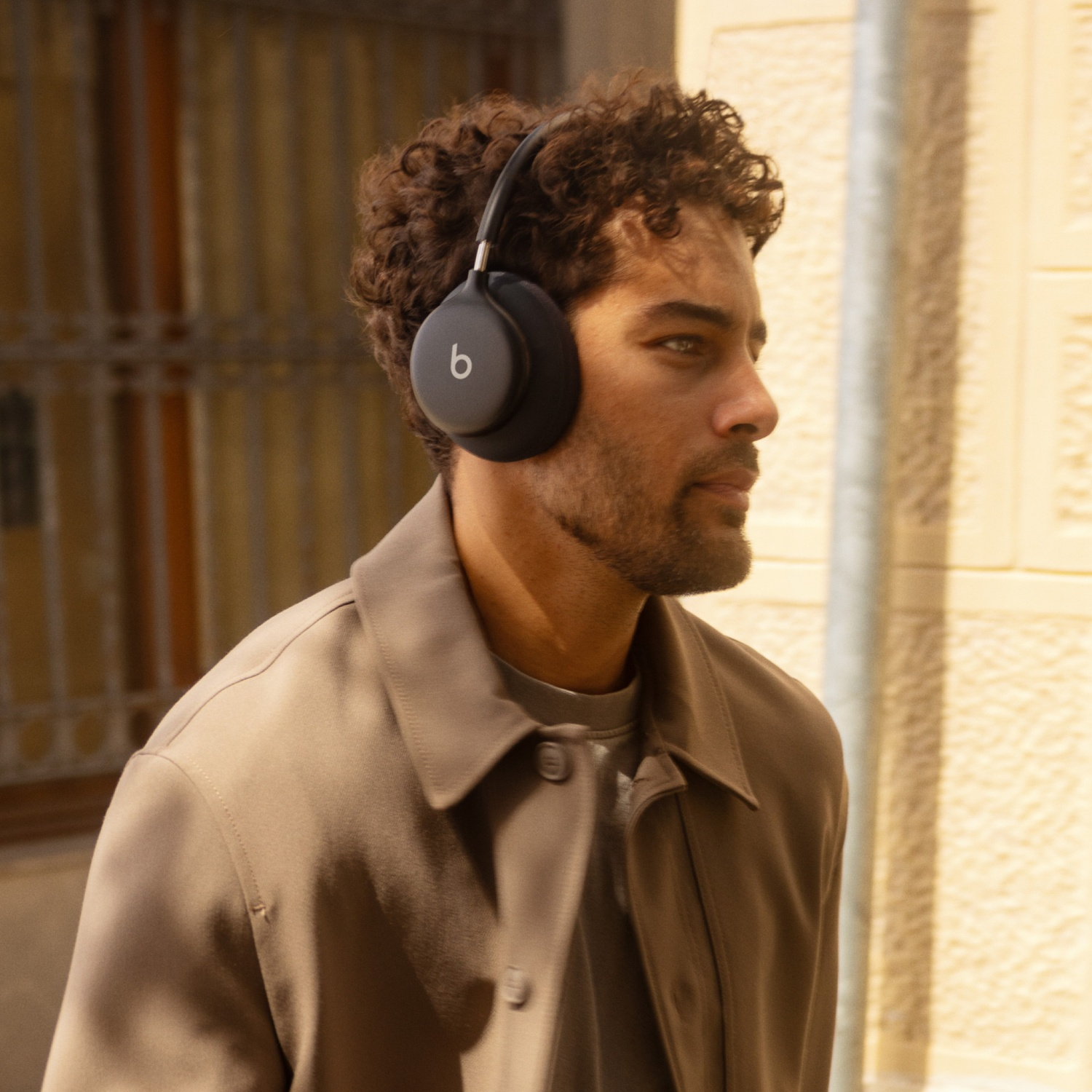 Un homme aux cheveux bouclés et veste marron porte un casque noir devant un mur.