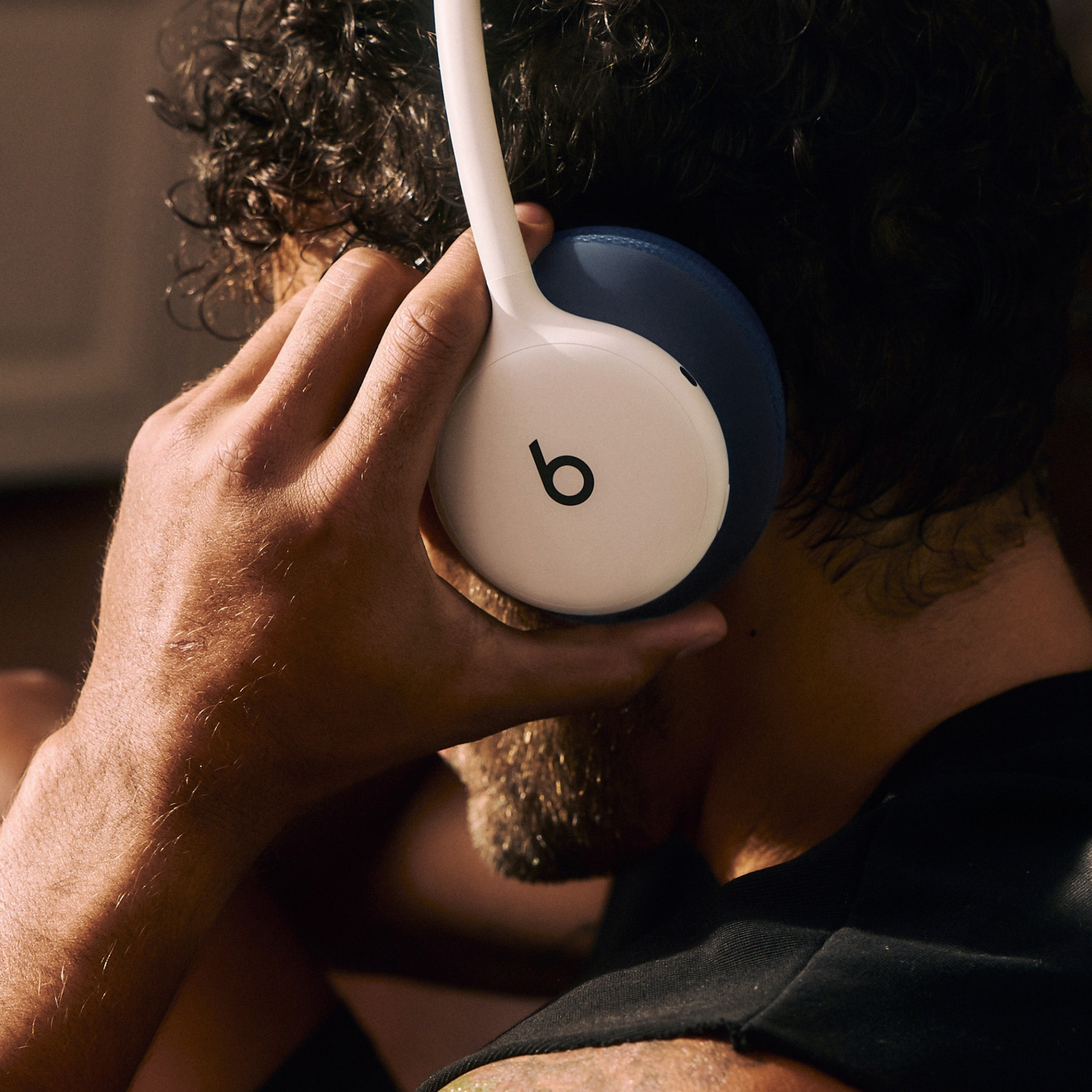 Un homme aux cheveux bouclés foncés ajuste des écouteurs blancs et bleus avec le logo Beats.