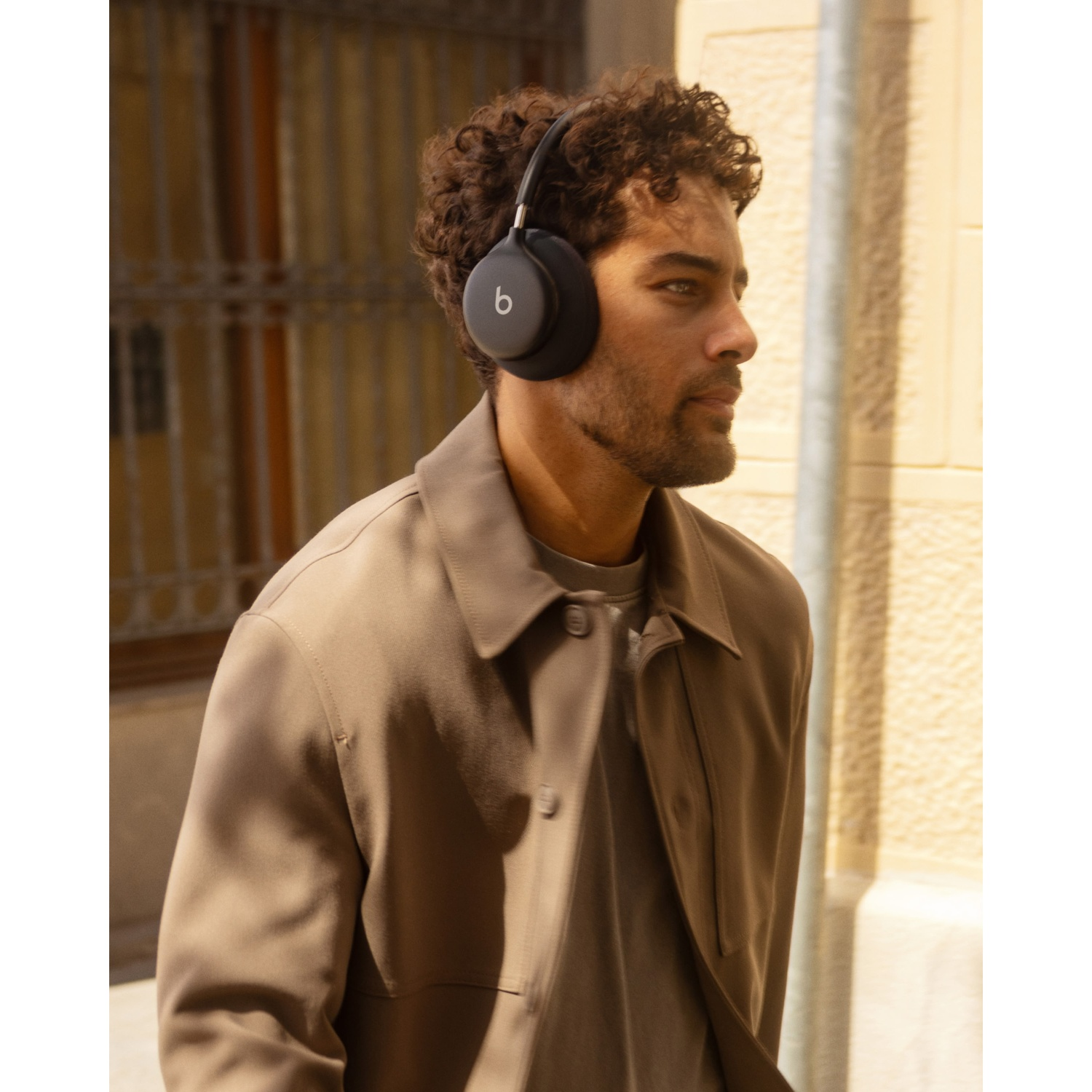 Un homme aux cheveux bouclés portant un casque sans fil noir et une veste marron.