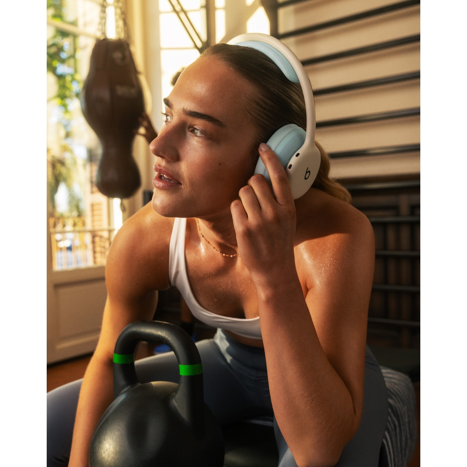 Une femme à la salle de sport portant un casque blanc et bleu, se reposant avec une kettlebell.