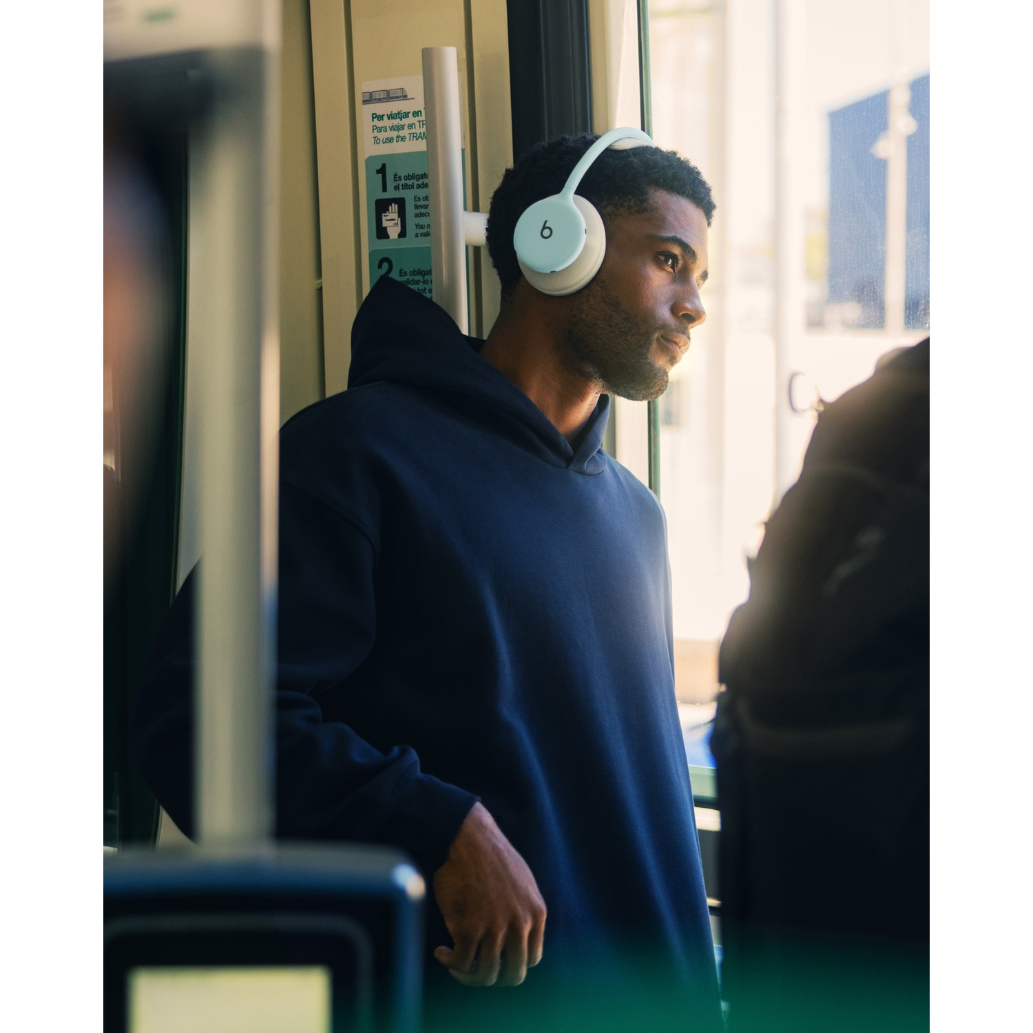Un jeune homme en sweat à capuche bleu et casque blanc regarde pensivement par la fenêtre dans les transports.