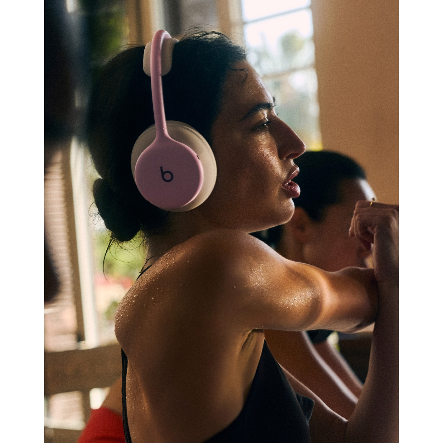 Une femme en sueur en tenue de sport portant un casque rose étire son bras à l'intérieur.