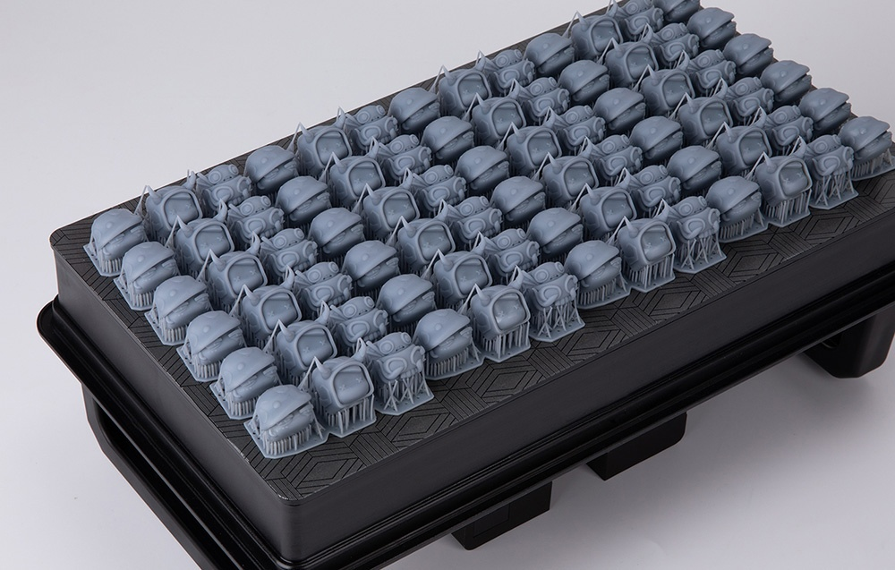Sorok apró, szürke, 3D-nyomtatott szörnyfigurákból szarvakkal egy fekete lapon.